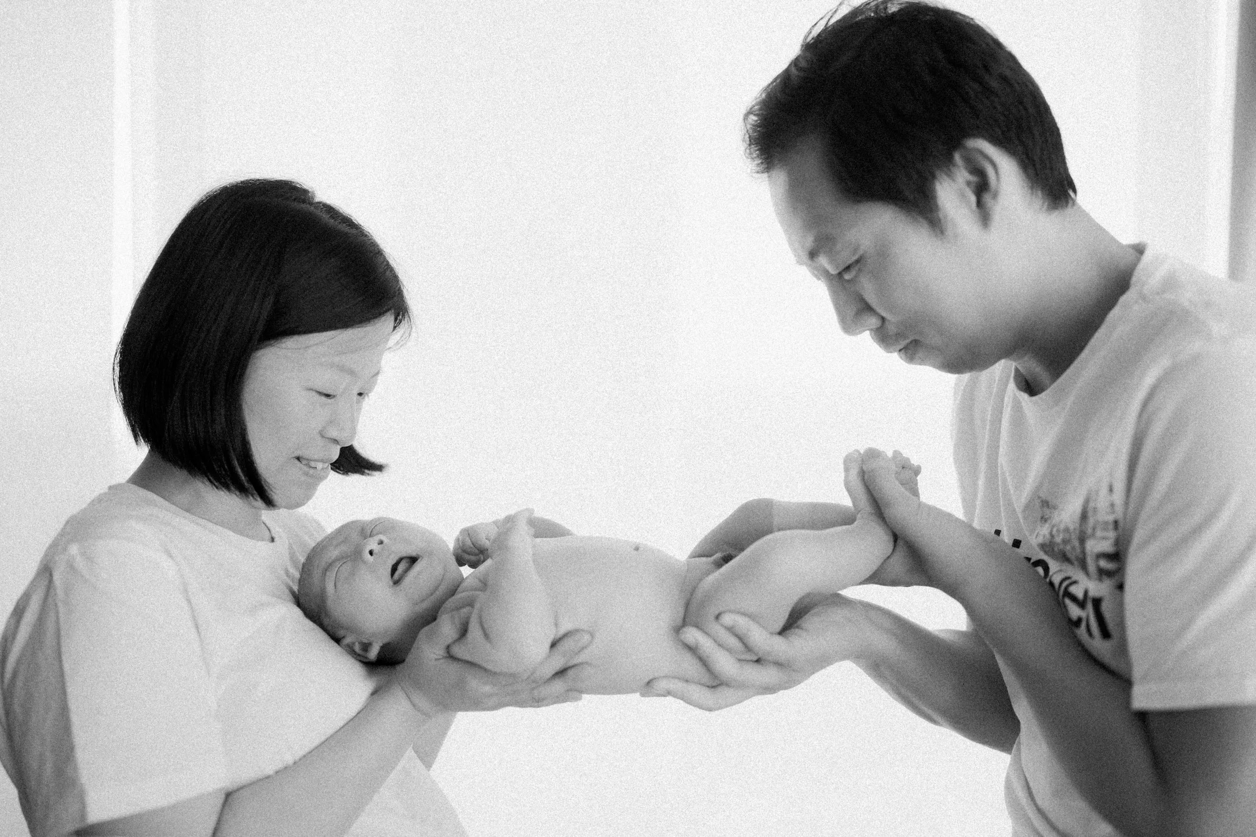  Mom and Dad admiring their newborn baby. Capturing the raw, emotional reality of early parenthood. 