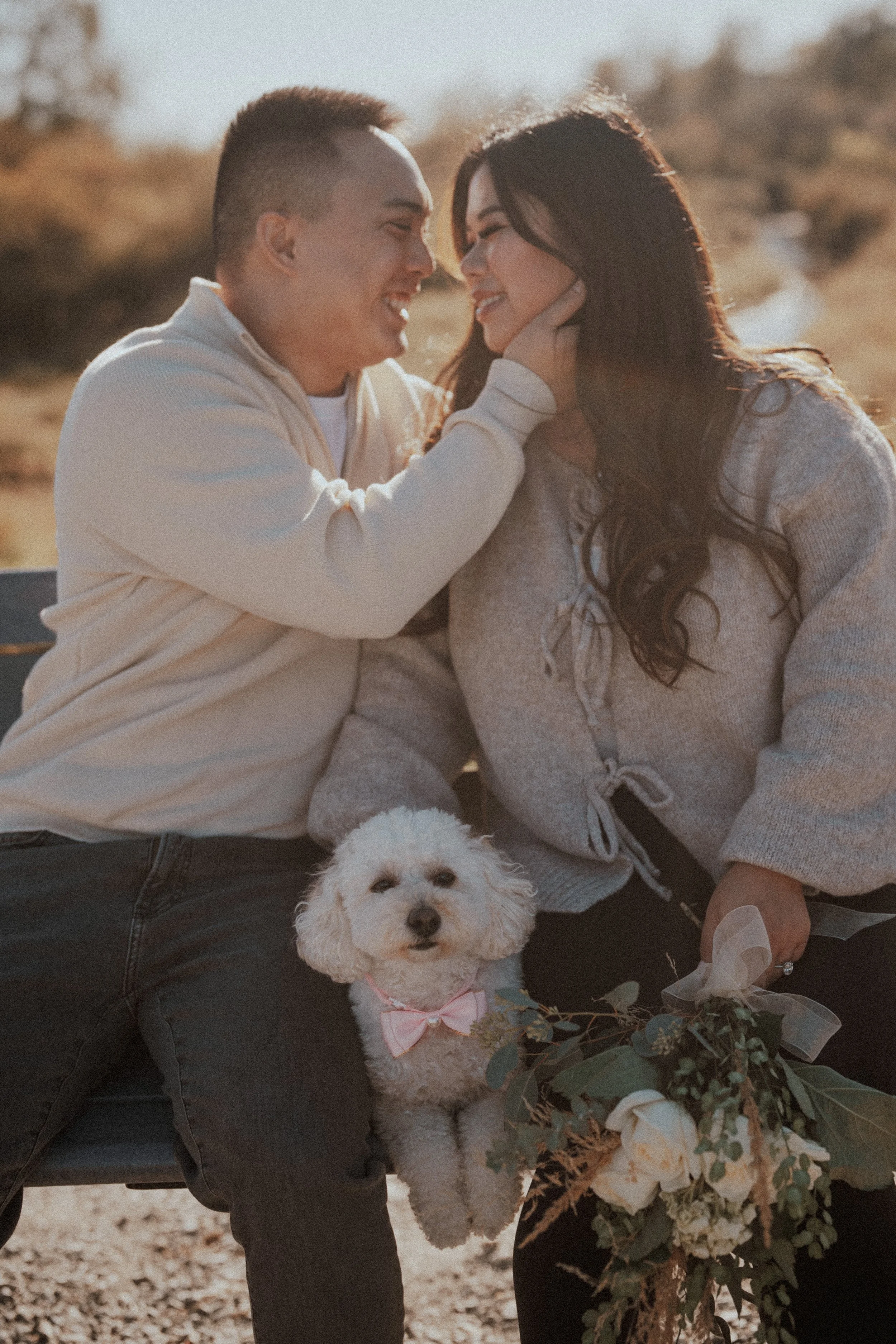  A heartwarming portrait of the couple and their dog, complete with a cute pink bow, sharing a moment on the bench. 