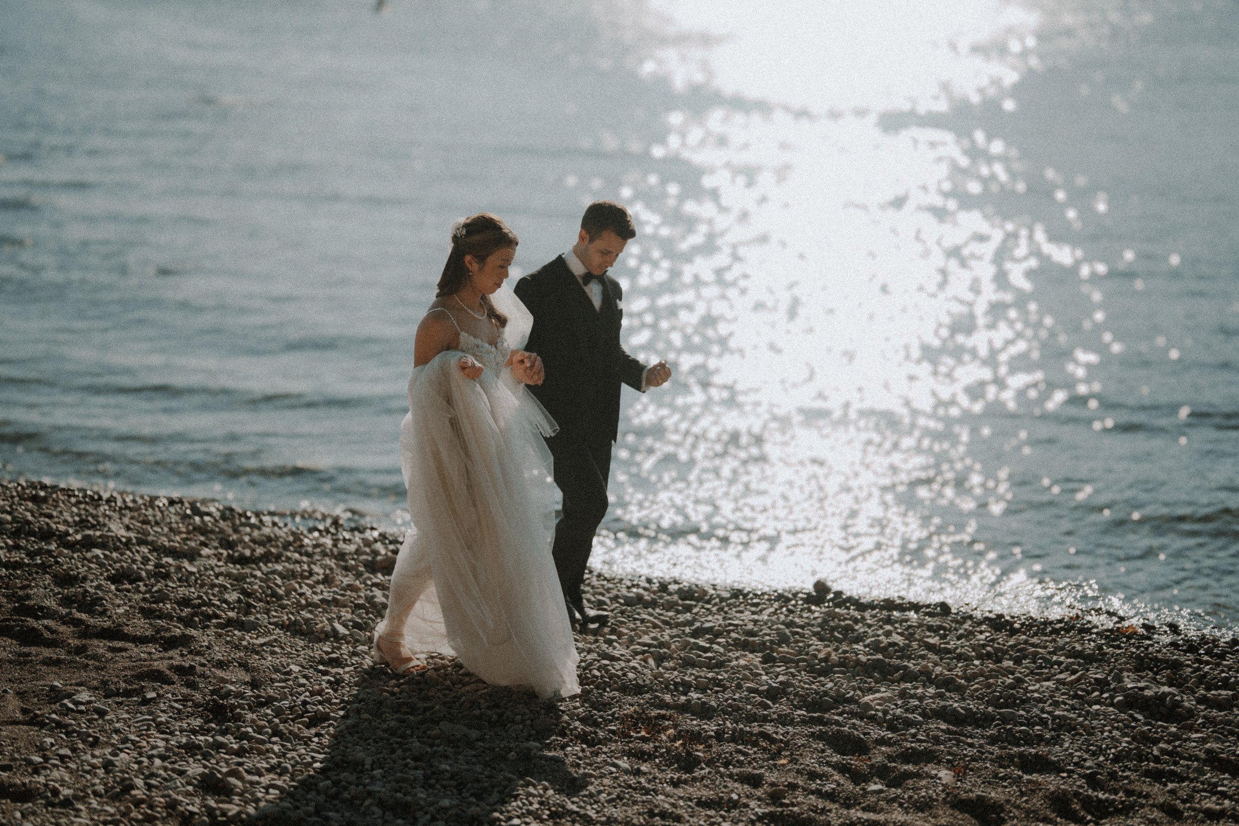  A beautiful moment on the  Vancouver  coastline. The couple walks along the pebble beach with the sun sparkling brightly on the water. 