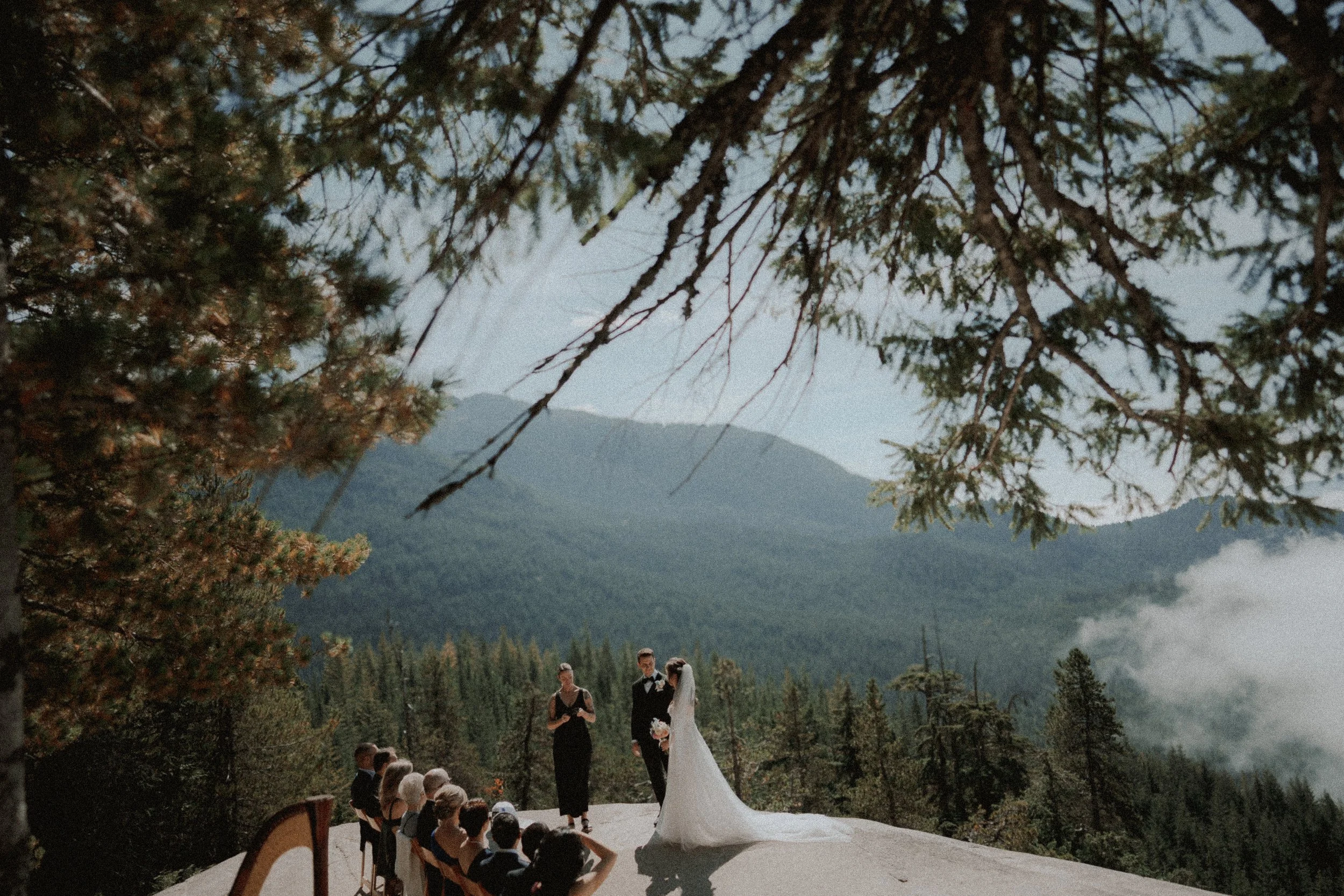  An intimate wedding ceremony high above the mountains at Sea to Sky Gondola. The couple stands on a rocky ledge, exchanging vows with a breathtaking view of the forest and sky. 