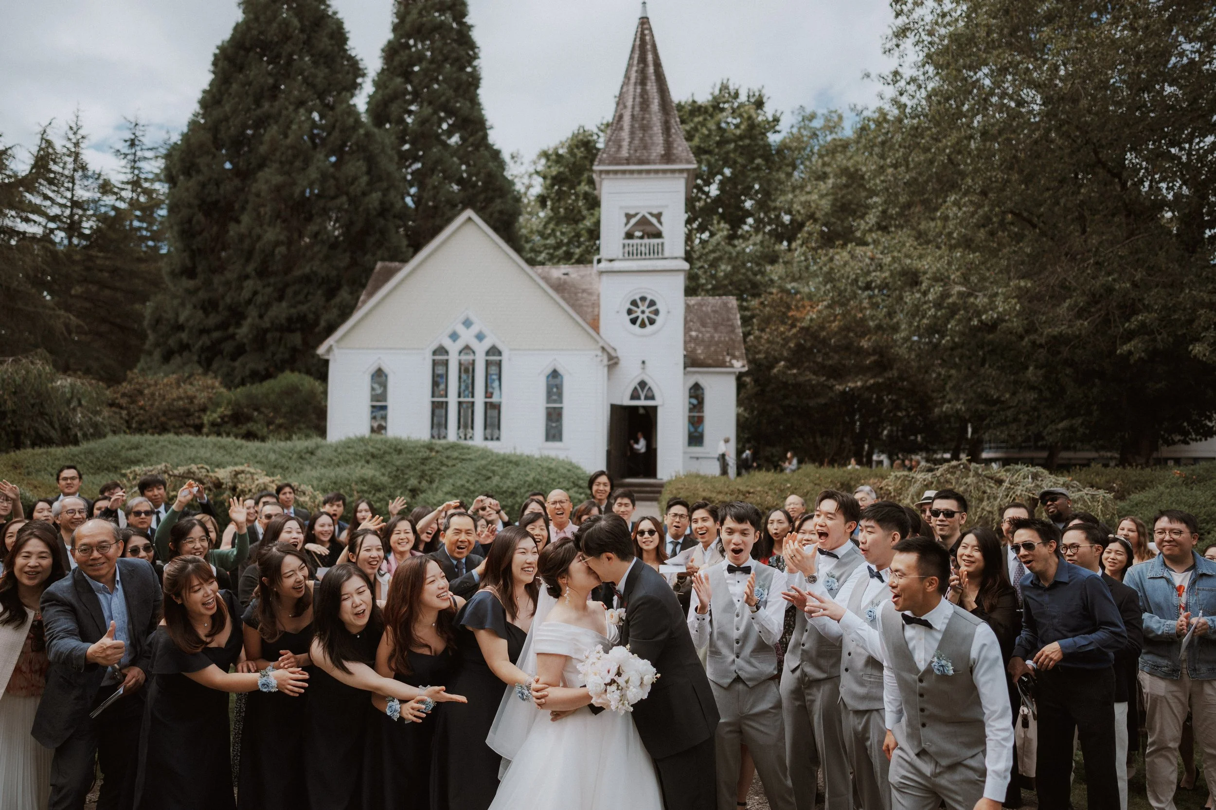  An iconic group photo! The newlyweds share a kiss, surrounded by a large crowd of family and friends celebrating outside the historic  Minoru Chapel . 
