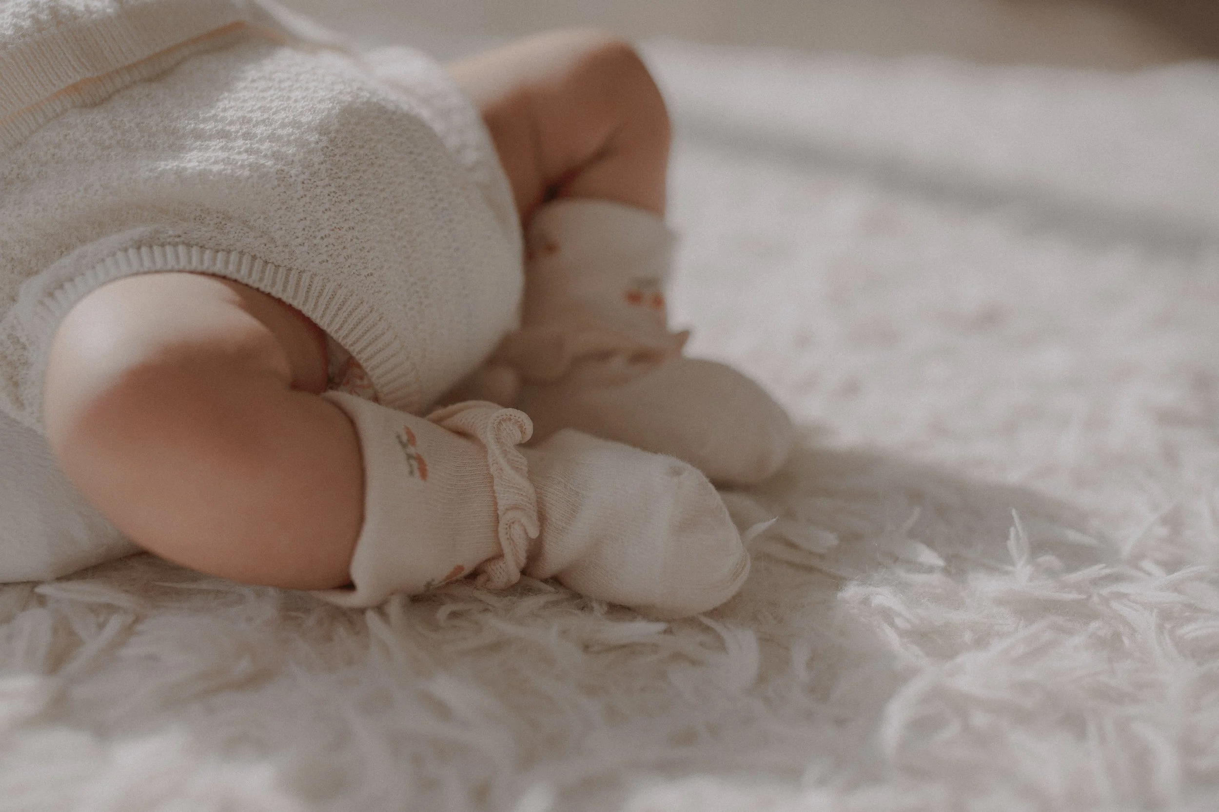 Close up of newborn baby wearing floral socks on a soft white rug captured in natural light with soft textures and earth tones for Tata and Lemon.