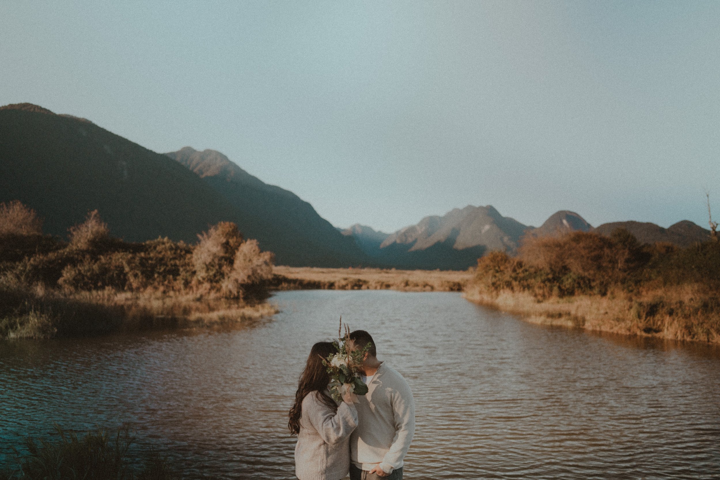  A tender kiss shared by the couple, framed by the subtle floral bouquet and the grand mountain scenery. 