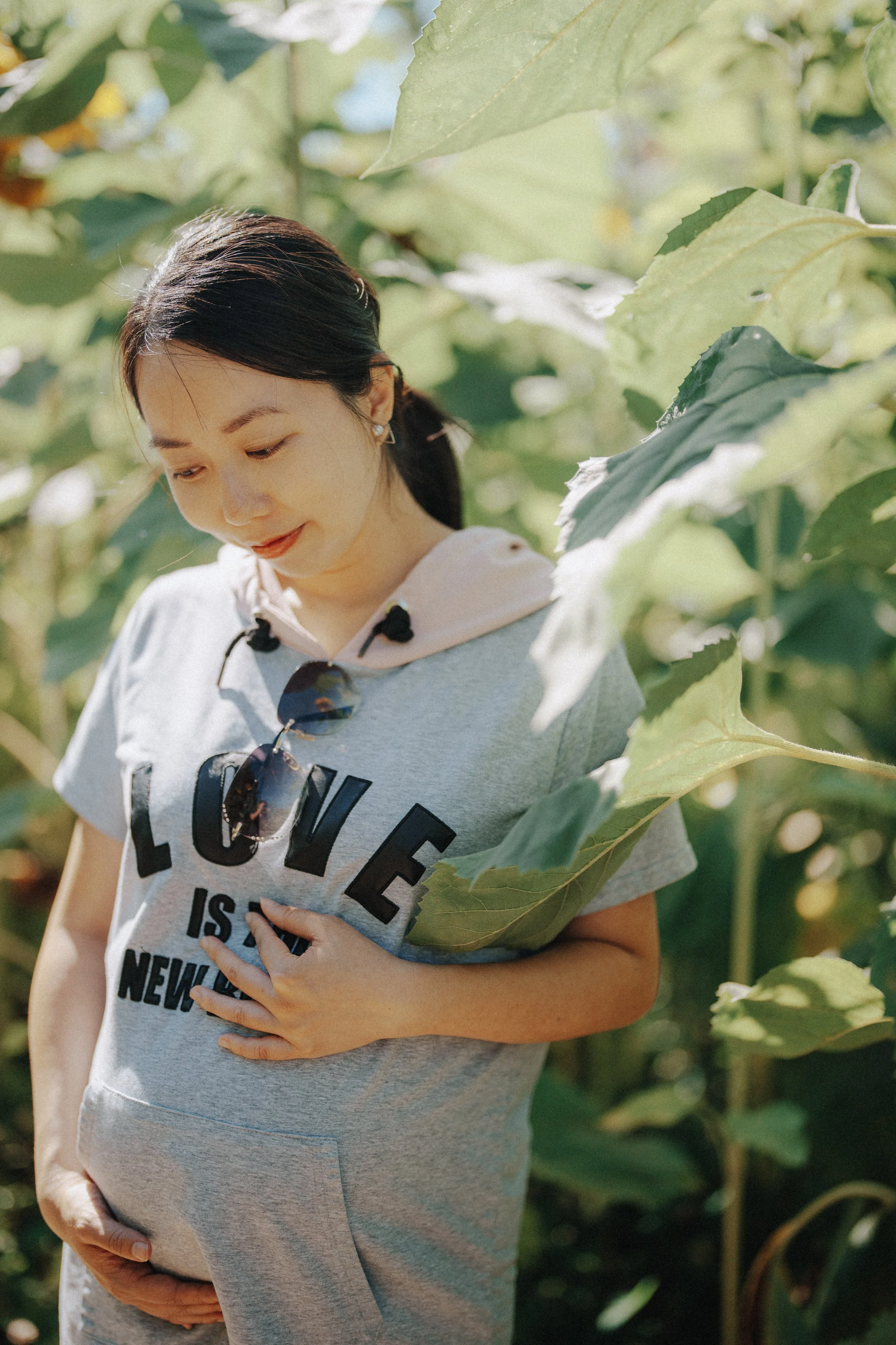  She stood quietly among the tall greens, hand on her belly, light catching her hoodie. It felt peaceful—like the garden was holding space for her. 
