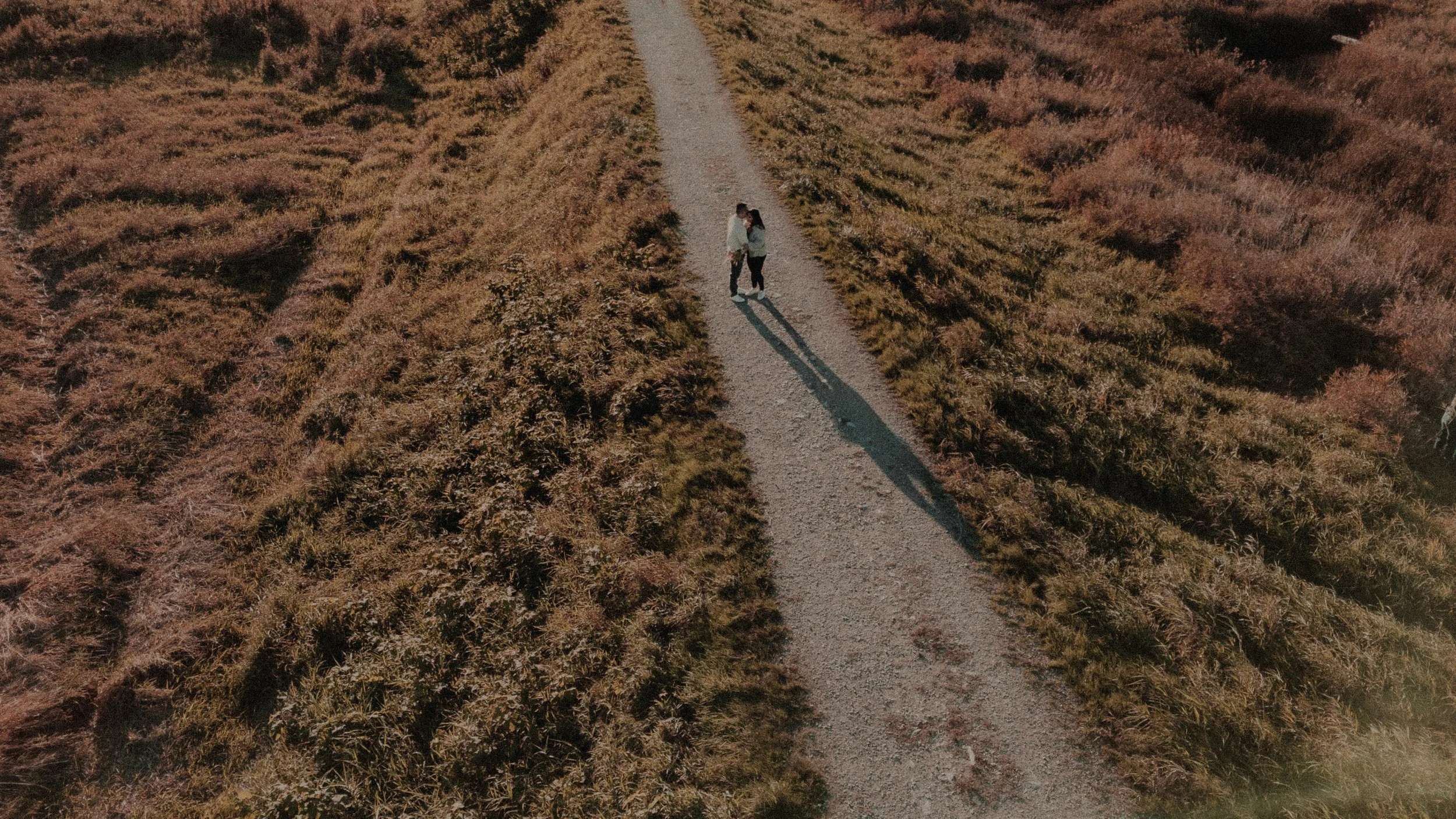  A beautiful, dramatic aerial view capturing the couple's walk and long shadows on the trail. 