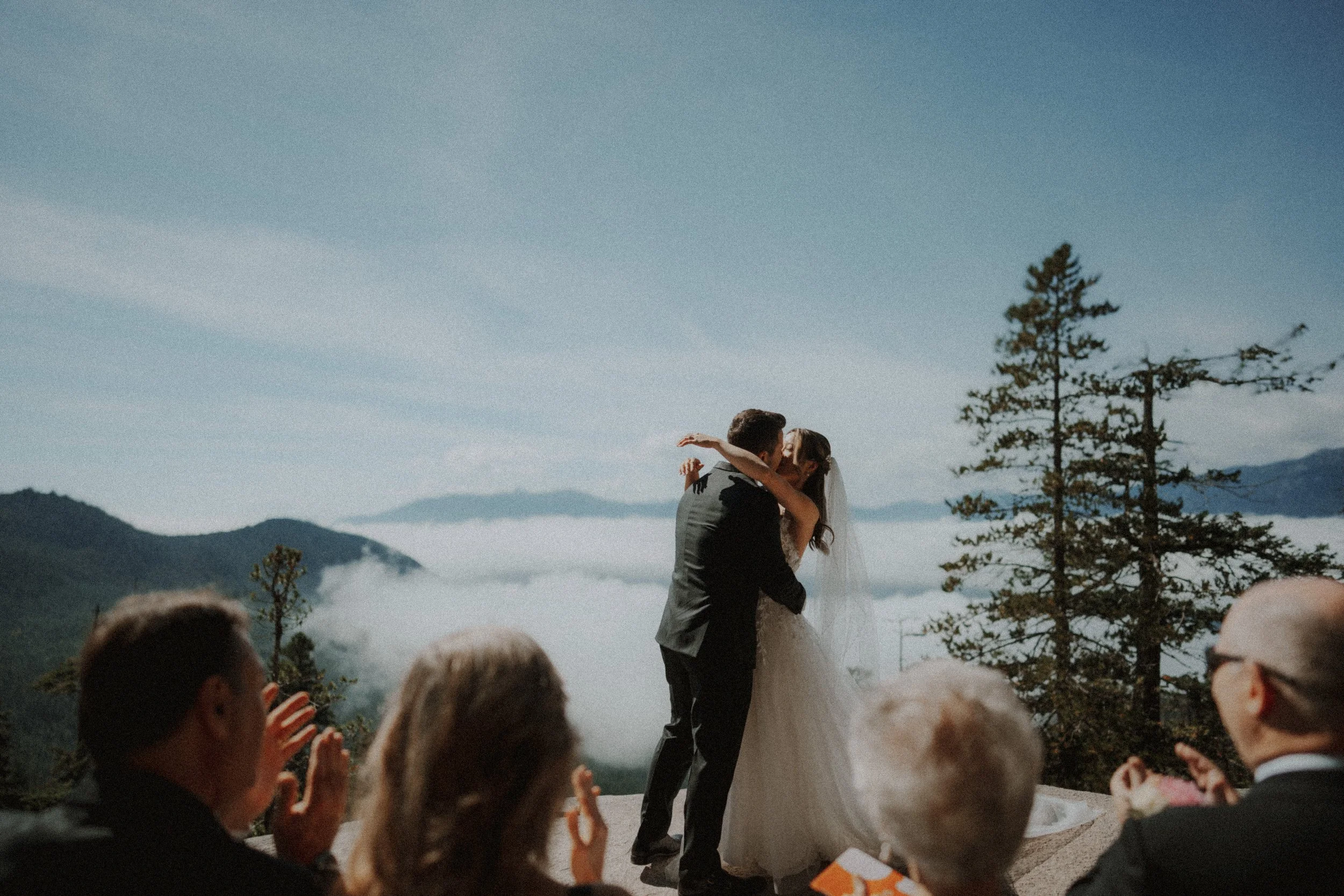  The perfect first kiss! The couple embraces on the mountain top, celebrating their marriage as the clouds fill the valley below. A stunning moment at their  Sea to Sky wedding . 