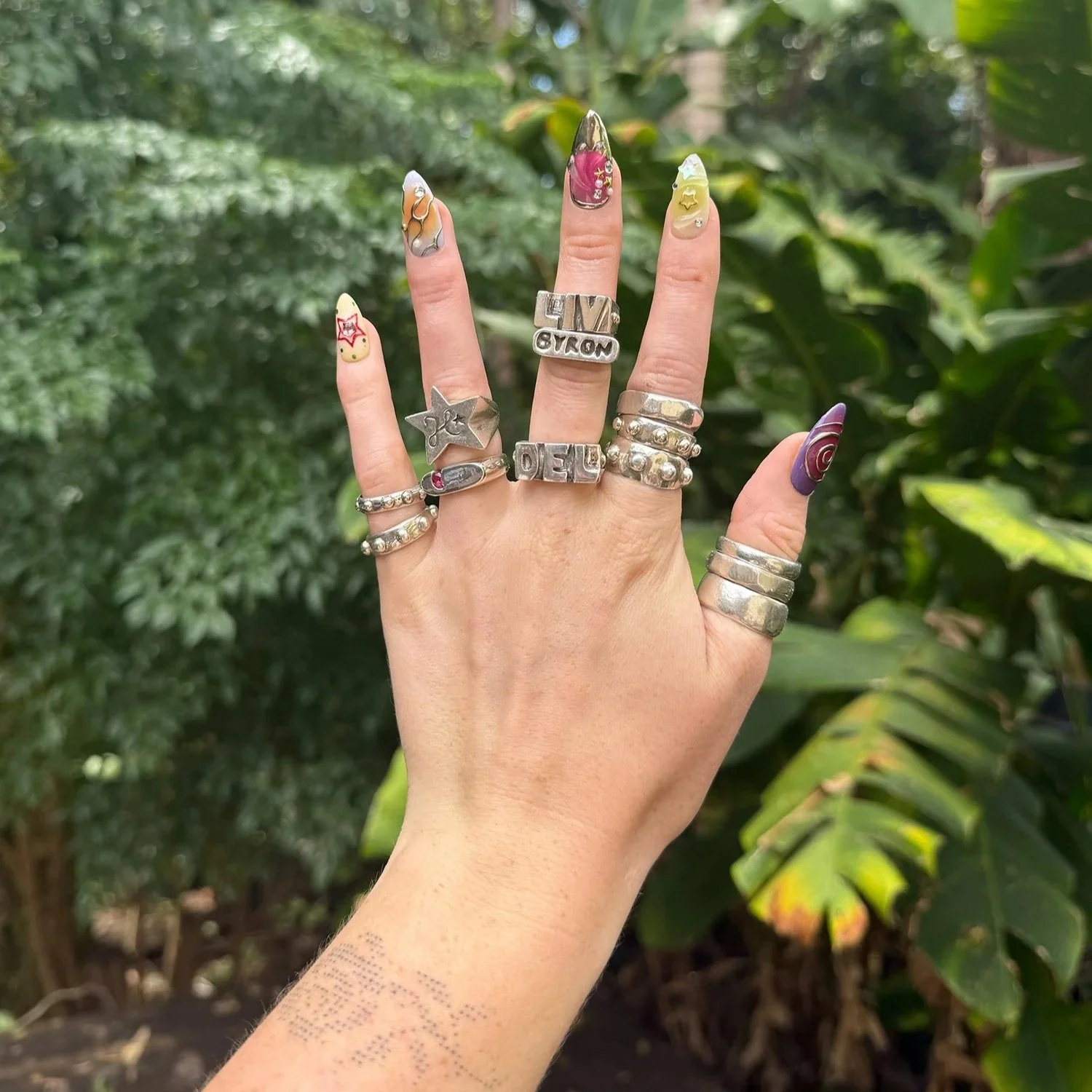 Chunky silver ring stack on hand with colourful nails.
