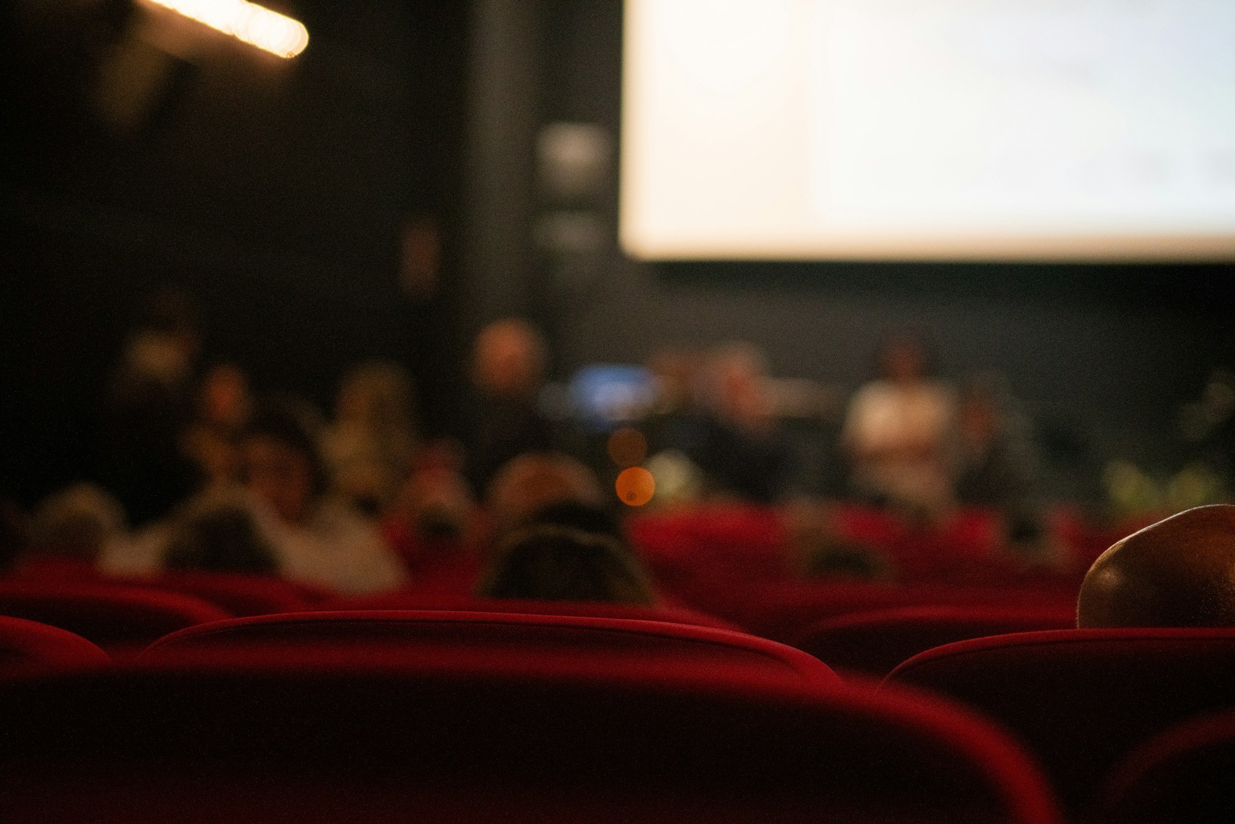 Mensen zitten in een donkere bioscoopzaal, gericht naar een groot scherm dat licht uitstraalt.