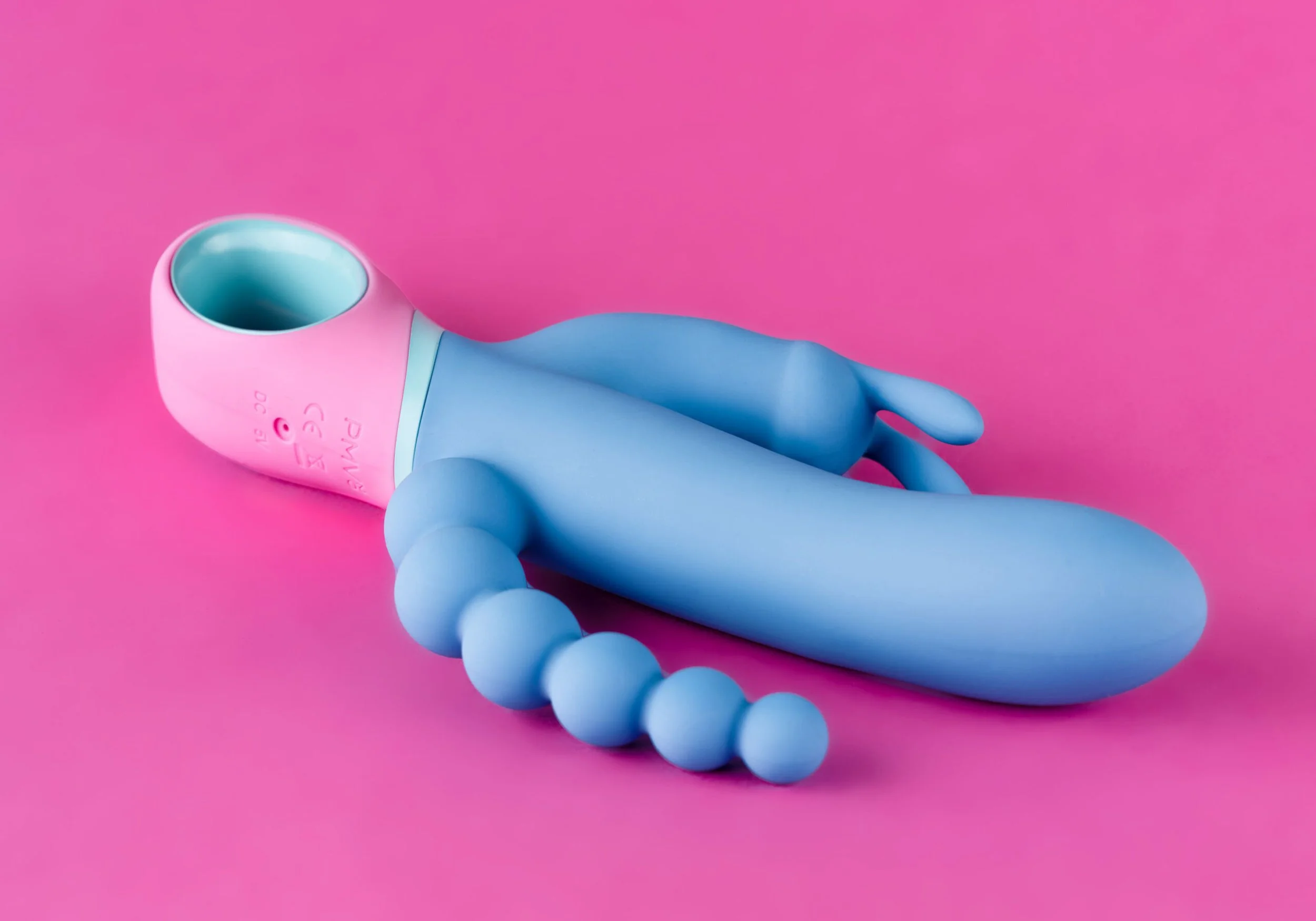 Een roze en blauwe Barbie-achtig speelding met een hol hoofd en een slijmachtige torso, met een rits en CE-markering, op een roze achtergrond.