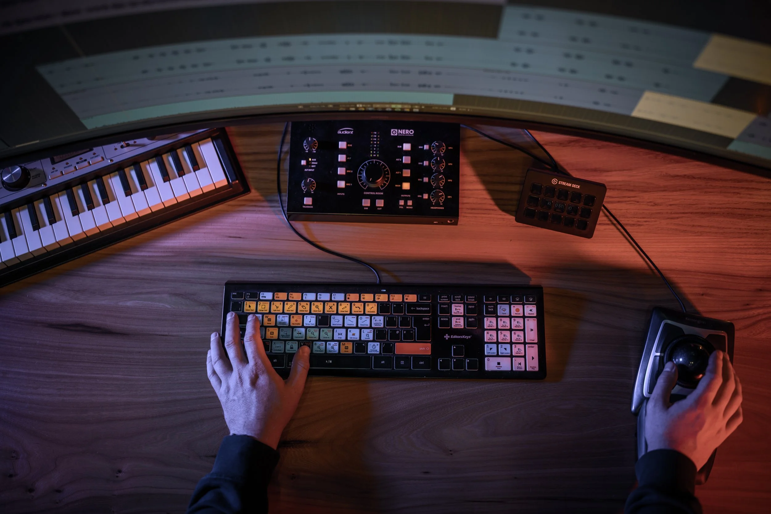 Bovenaanzicht van een audioproductiewerkplek bij Kudo Media met MIDI-keyboard, mengpaneel, Stream Deck en verlicht toetsenbord