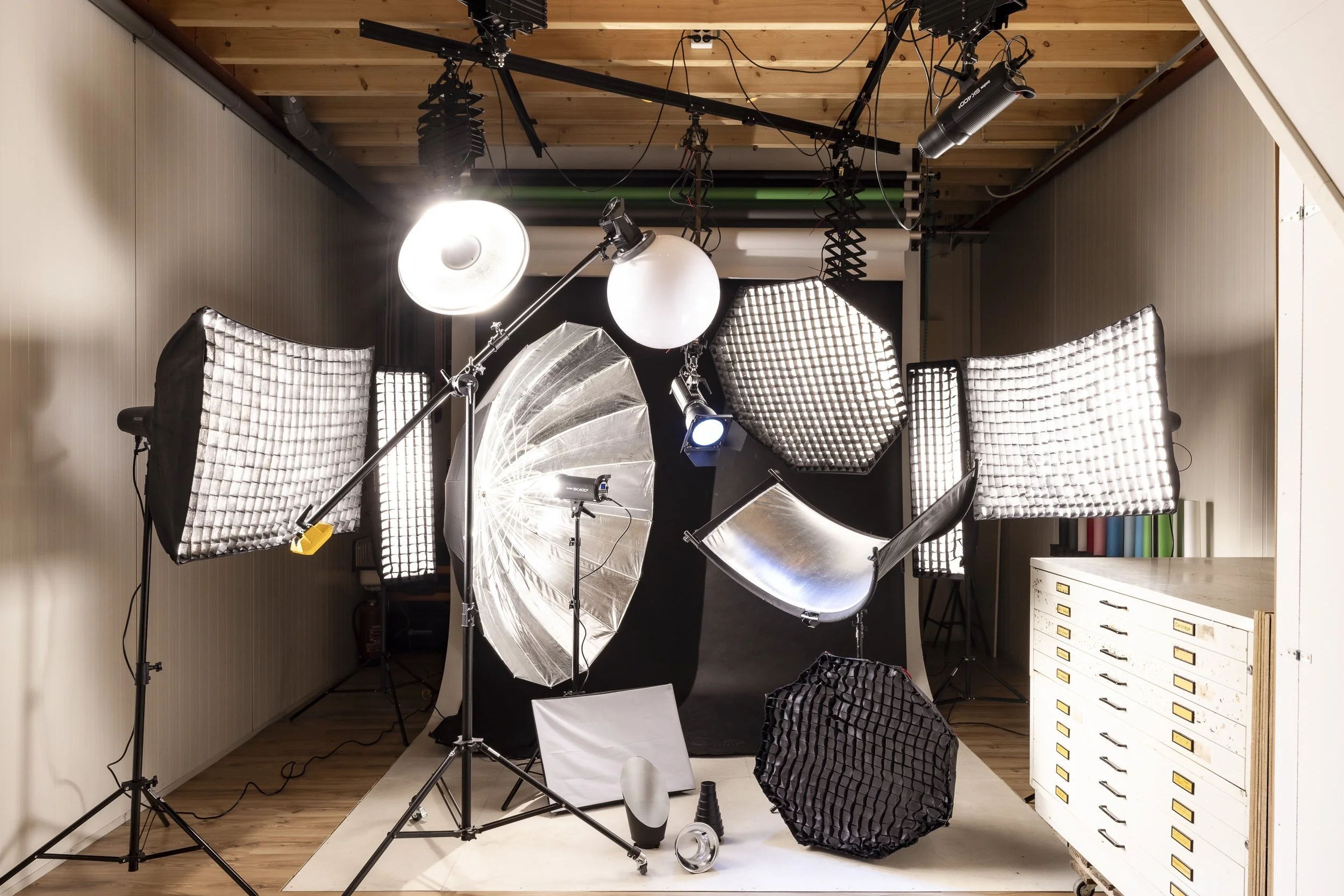Fotostudio van kudo media met diverse studioverlichting en apparatuur, inclusief paraplu's, softboxen, en reflectoren, klaar voor fotoshoot.