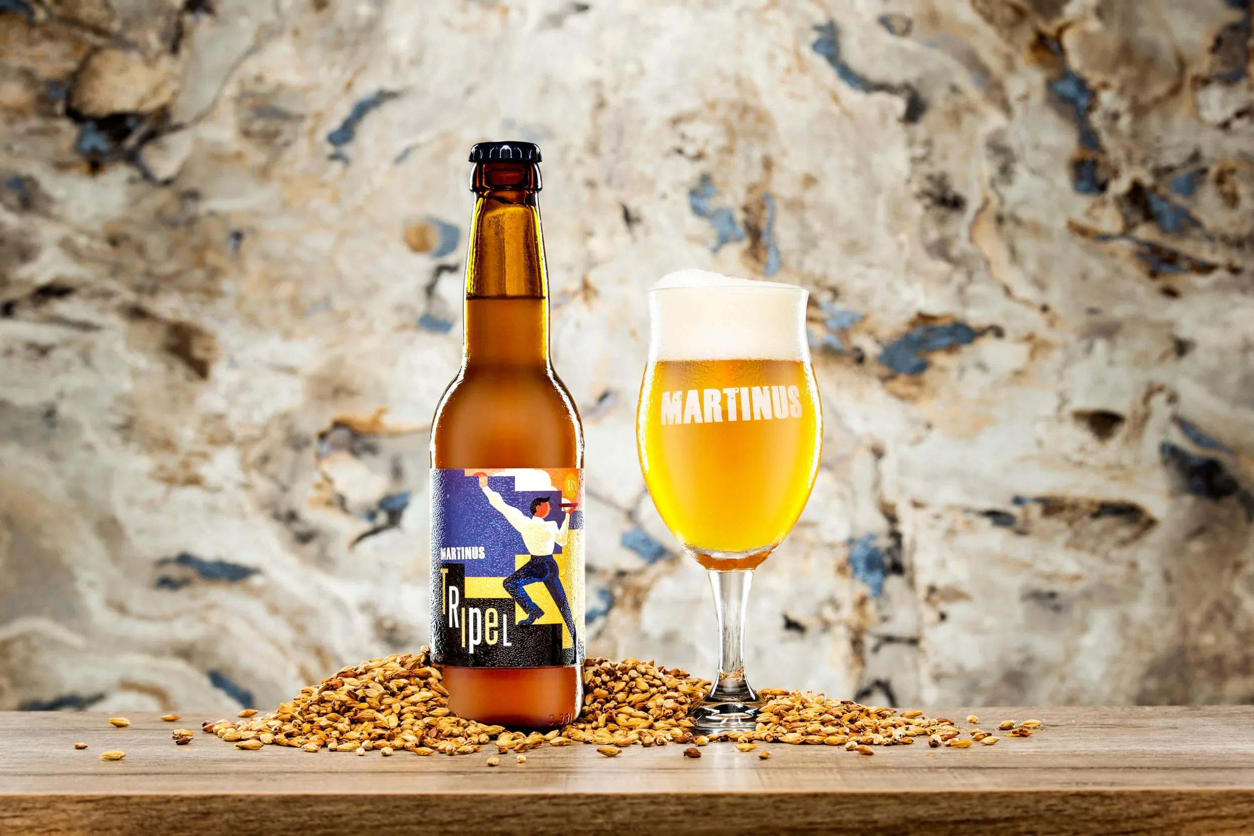 Een Flesje Martinus Bier uit Groningen en glas bier op houten tafel met gerst en een stenen muur op de achtergrond.