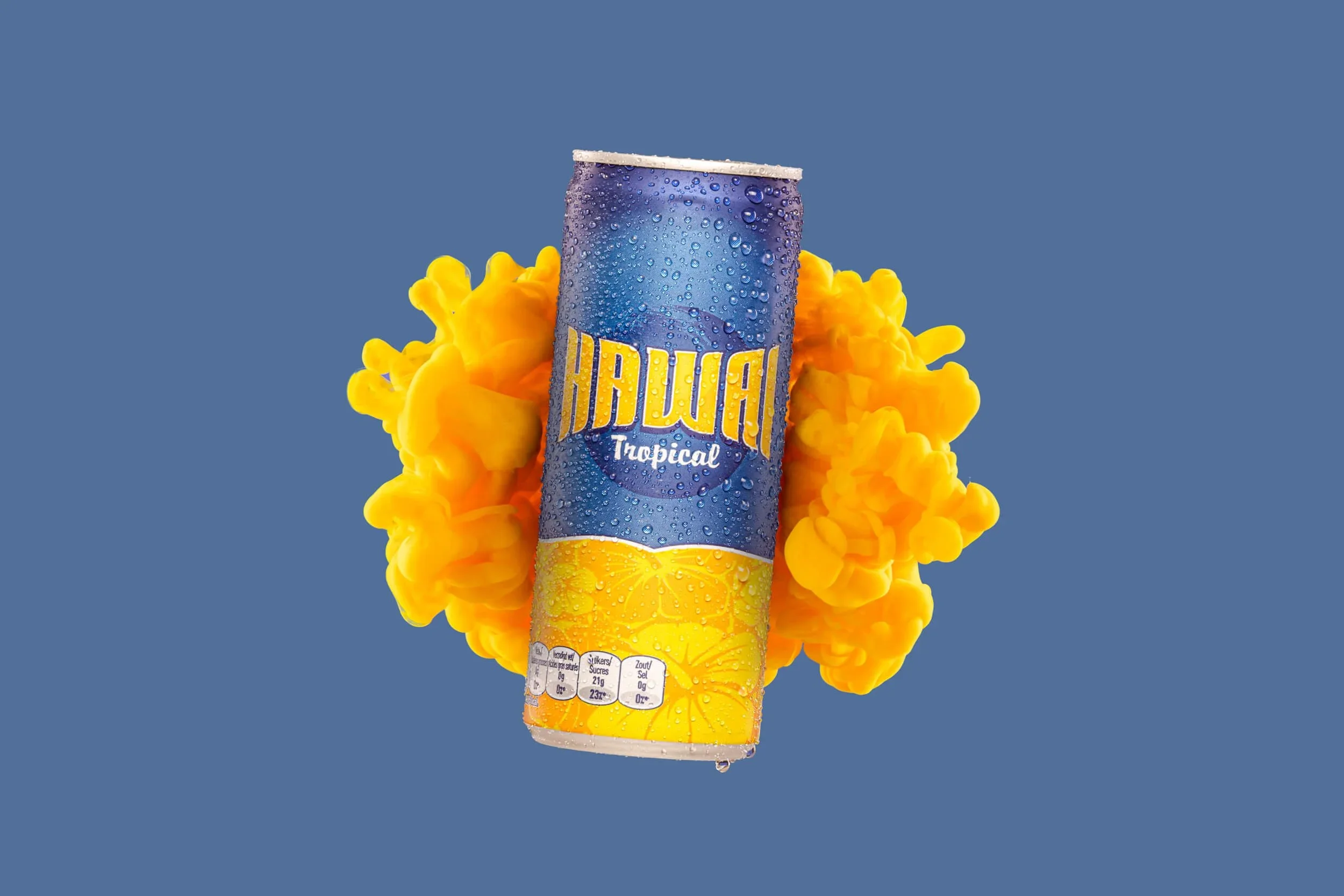 Een blikje Hawai Tropical met waterdruppels op het oppervlak, omringd door een gele en oranje rook of inktwolken op een blauwe achtergrond.