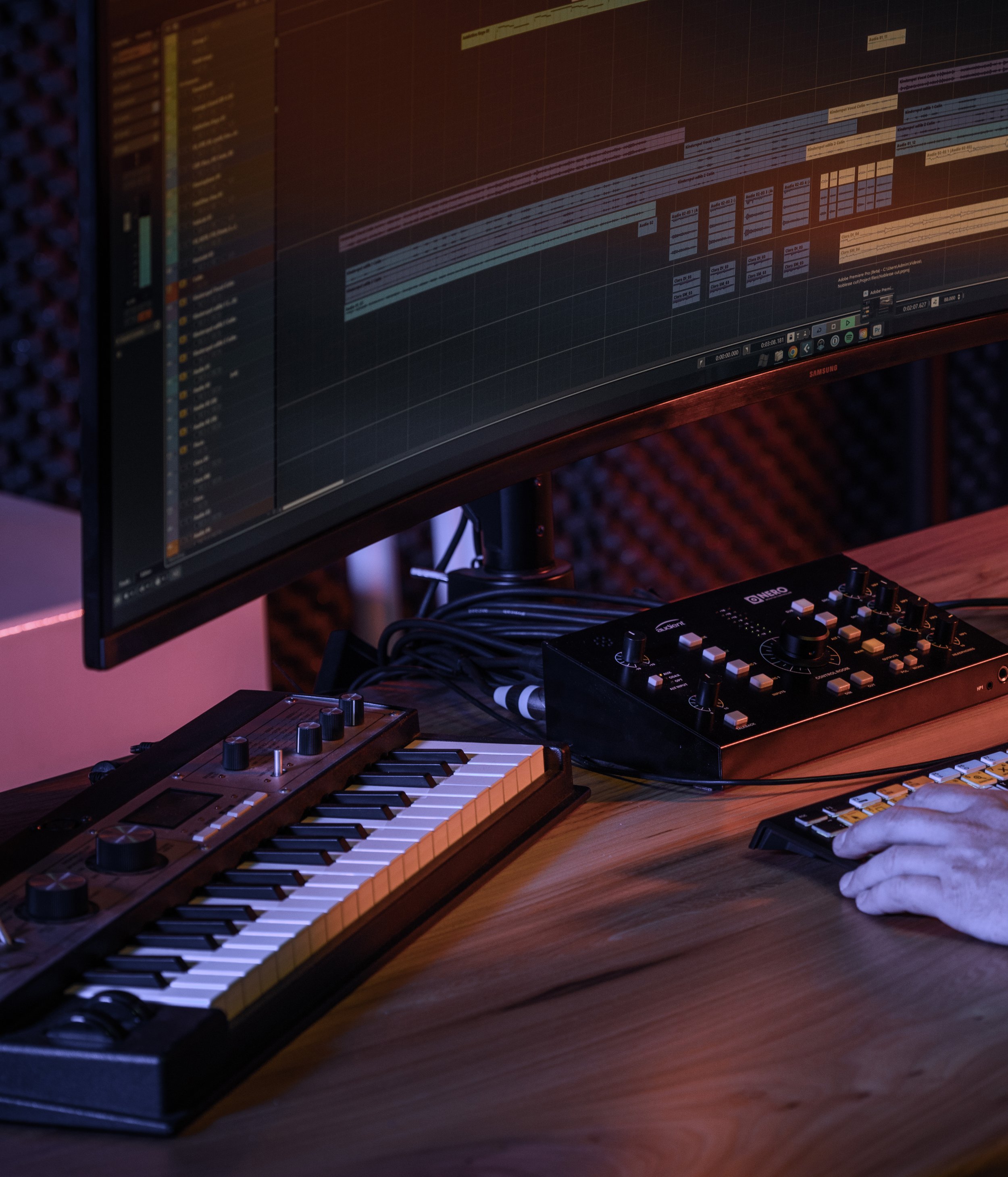 Audioproductie in de studio van Kudo Media met DAW-tijdlijn op een breedbeeldmonitor, synthesizer, mengpaneel en producer aan het werk