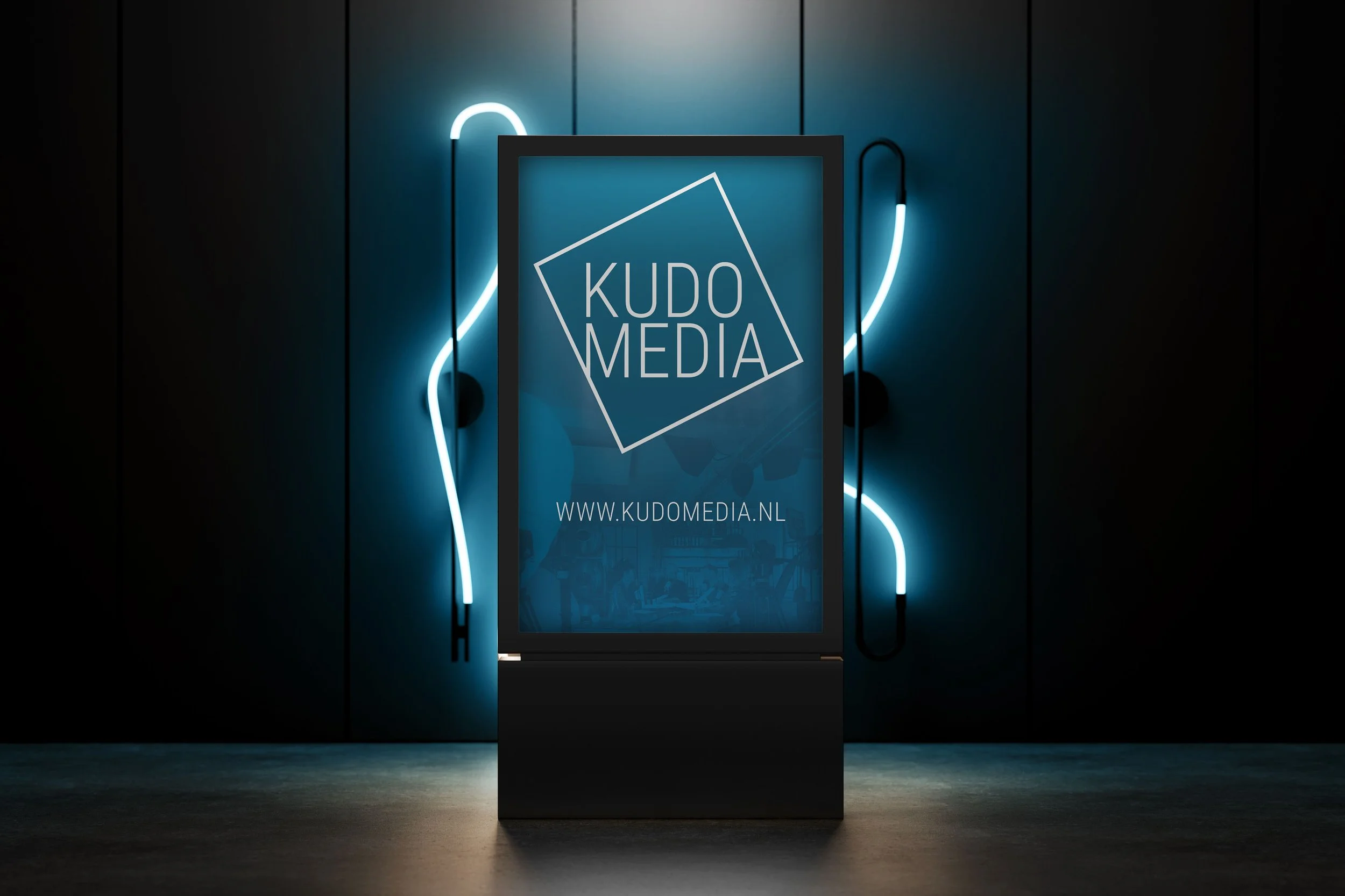 Verlichte reclamebord voor KUDO MEDIA met website URL, tegen een donkere muur met neonlichtaccenten.