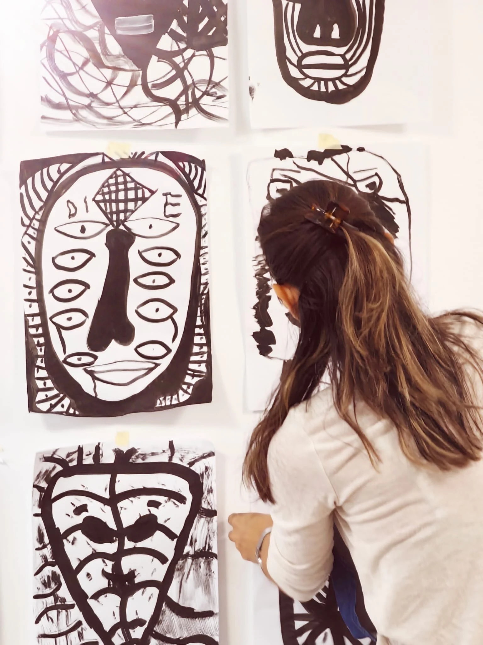 A woman with long brown hair, secured with a large hair clip, is observing black and white abstract drawings on a wall.