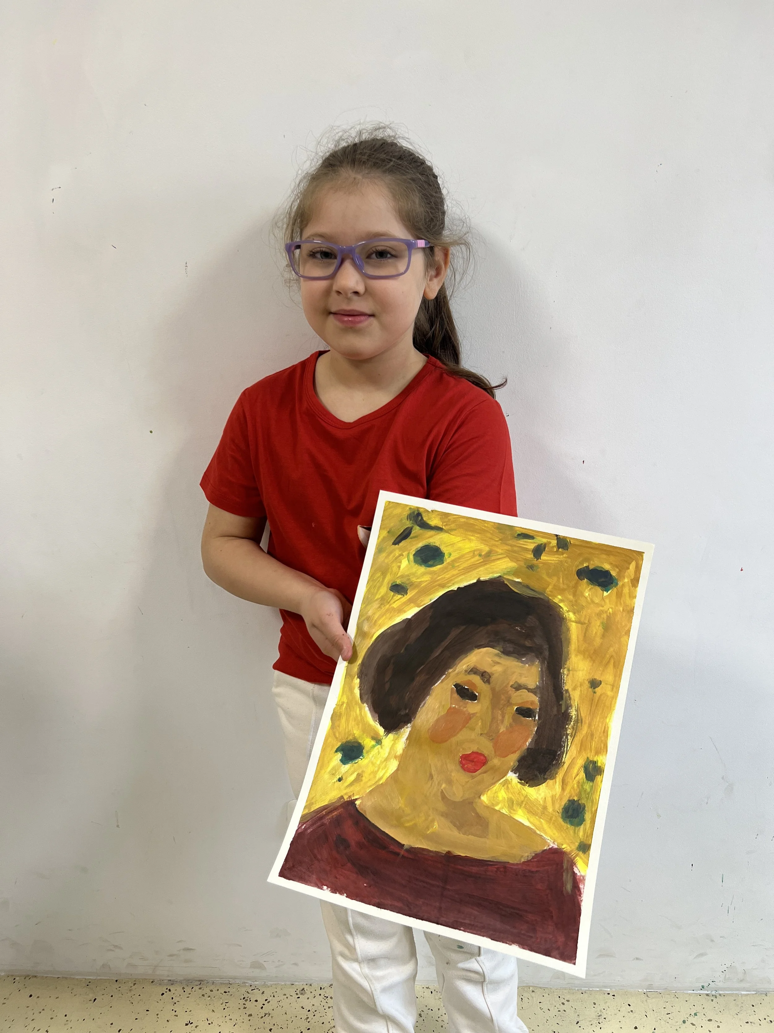 Young girl with glasses holding a painting of a woman with dark hair and red lips, set against a yellow background with green dots.