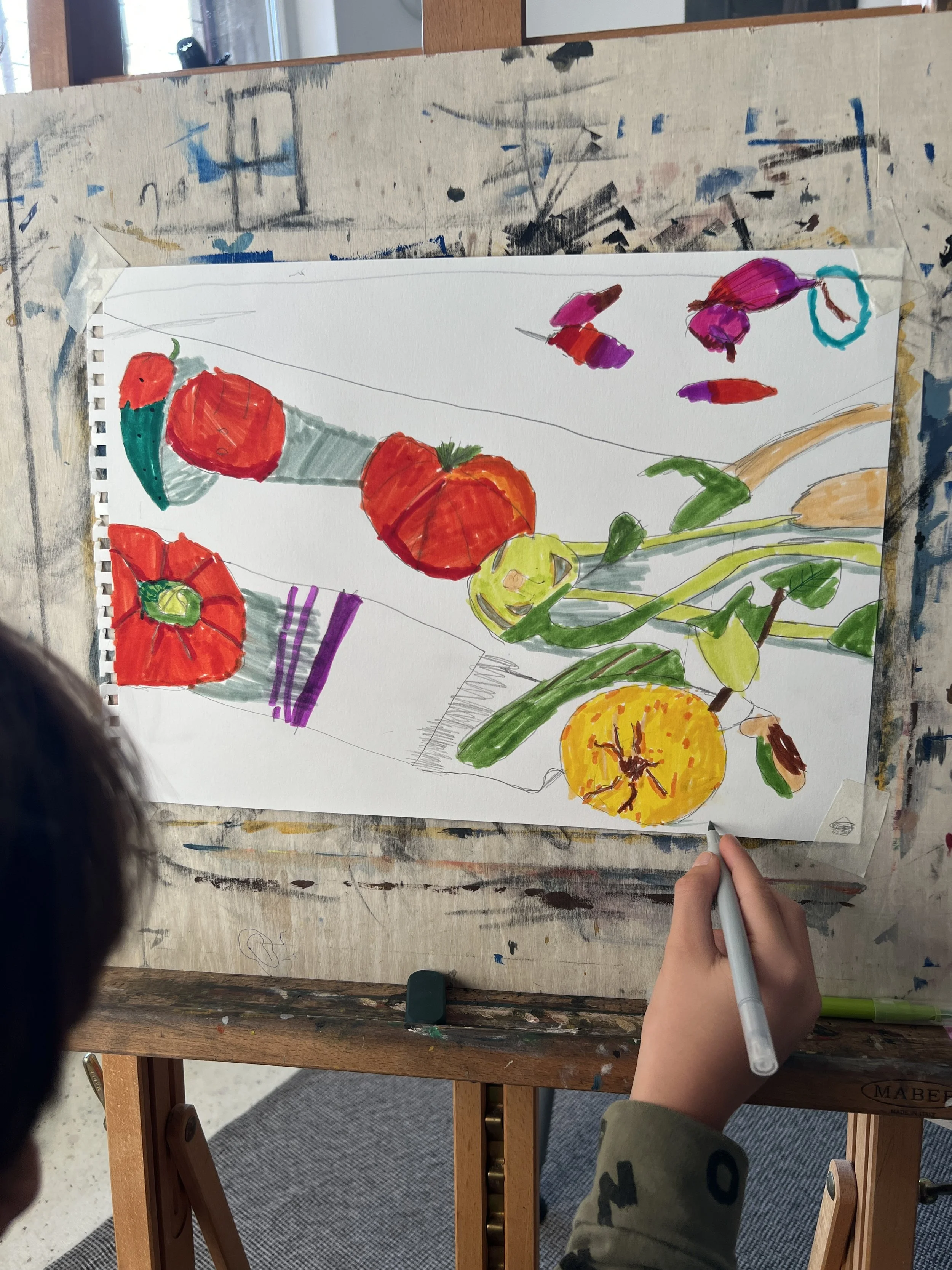 A colorful drawing of various vegetables, including tomatoes, a cucumber, and a pumpkin, created with markers on a white sheet of paper taped to an easel.