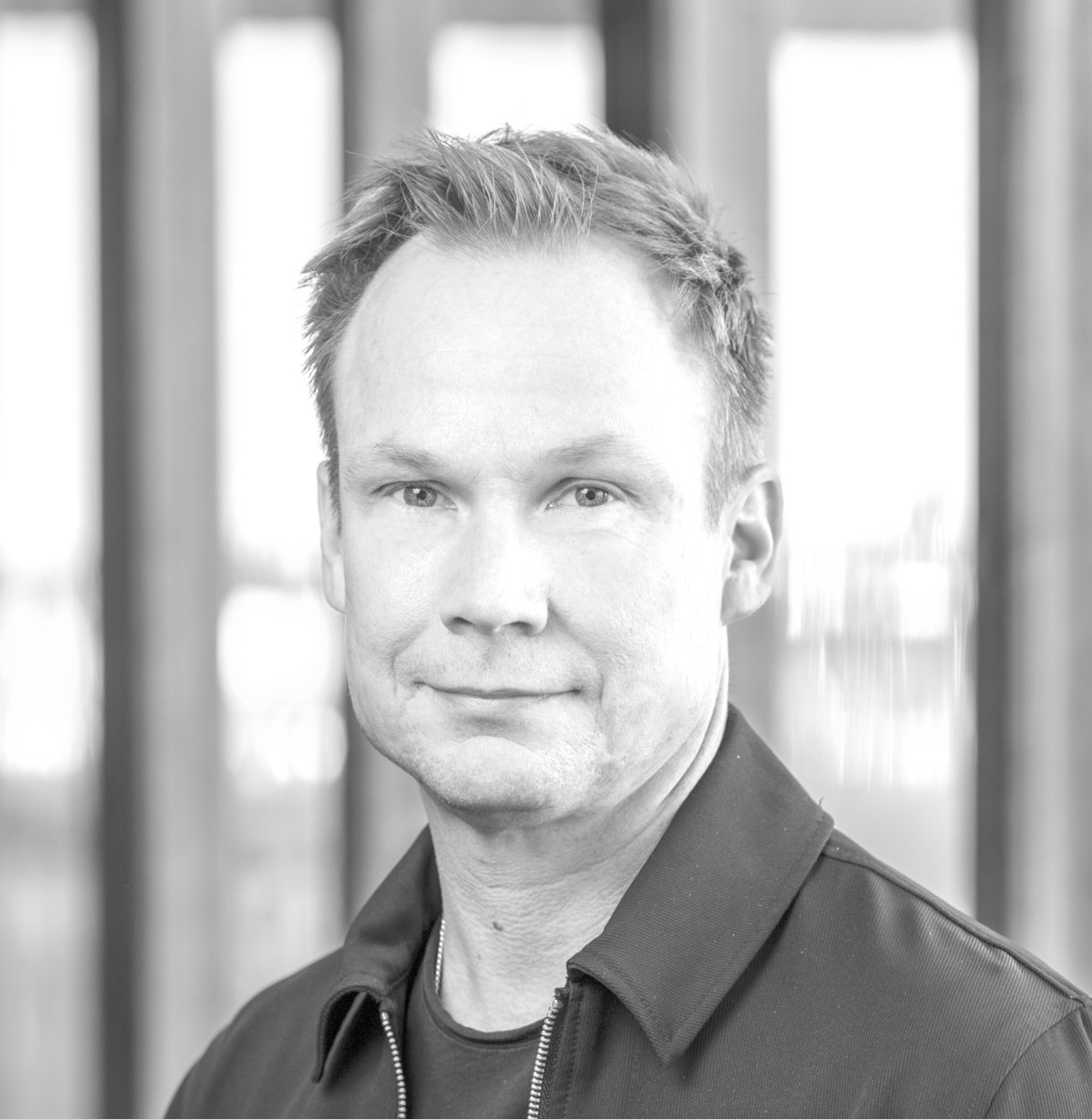 A man outdoors taking a selfie with a brick wall and leafy tree in the background.