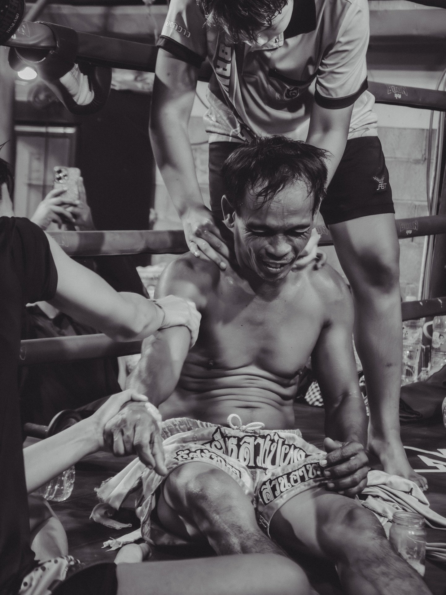 Teenage fighters apply ya mong, a traditional herbal liniment, to one of their coaches at Por Muangphet Gym. The coach, a former fighter, oversees the training of 6 athletes twice daily, moving between pad work, conditioning, and supervision througho