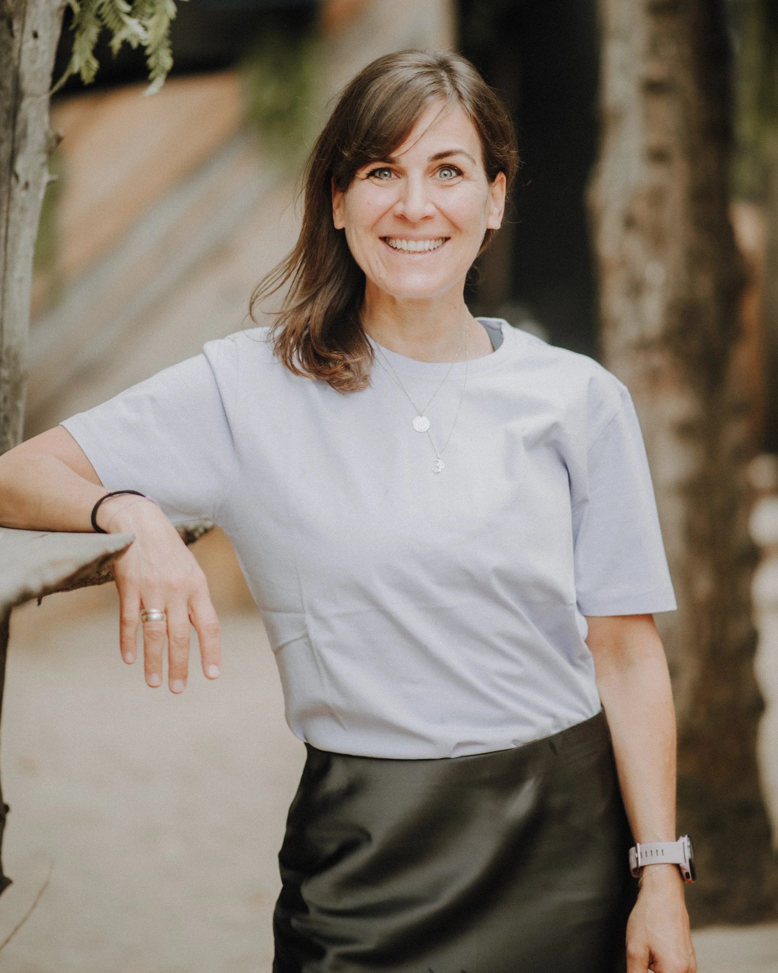 Our trainer Katharina sits relaxed outside on the side of a building, wearing sportswear and smiling at the camera.