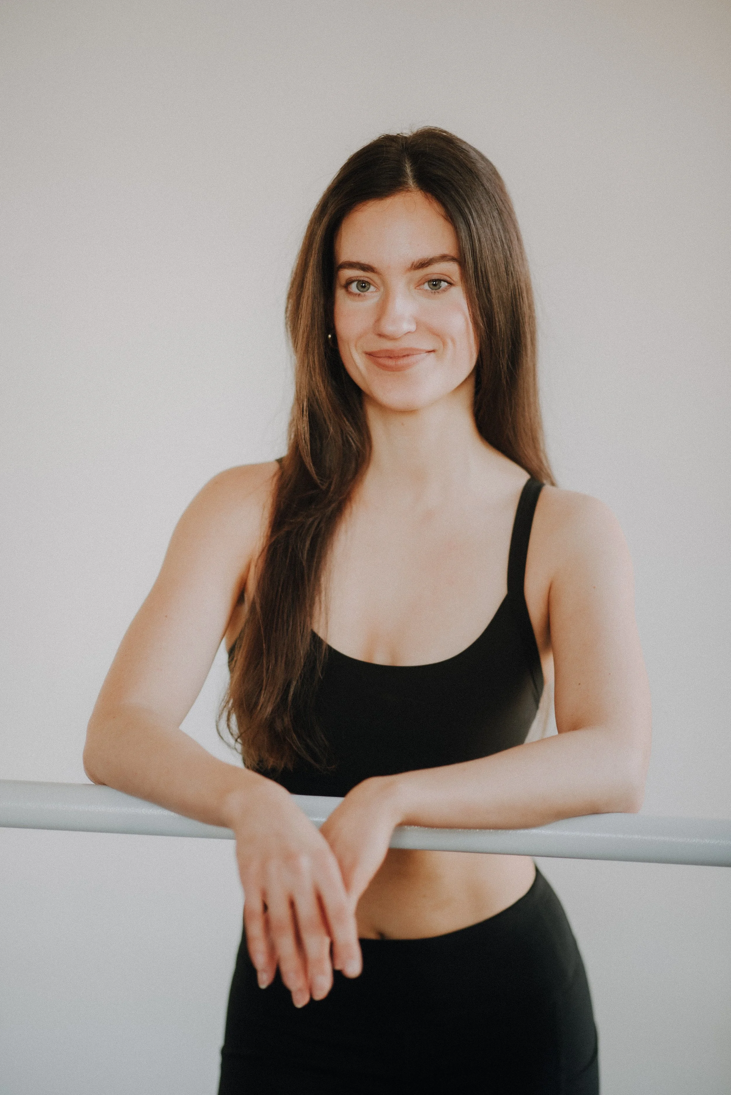 Unsere Trainerin Camilla mit dunklen, lockigen Haaren, in einem lilafarbenen Sporttop, vor einer weißen Wand.