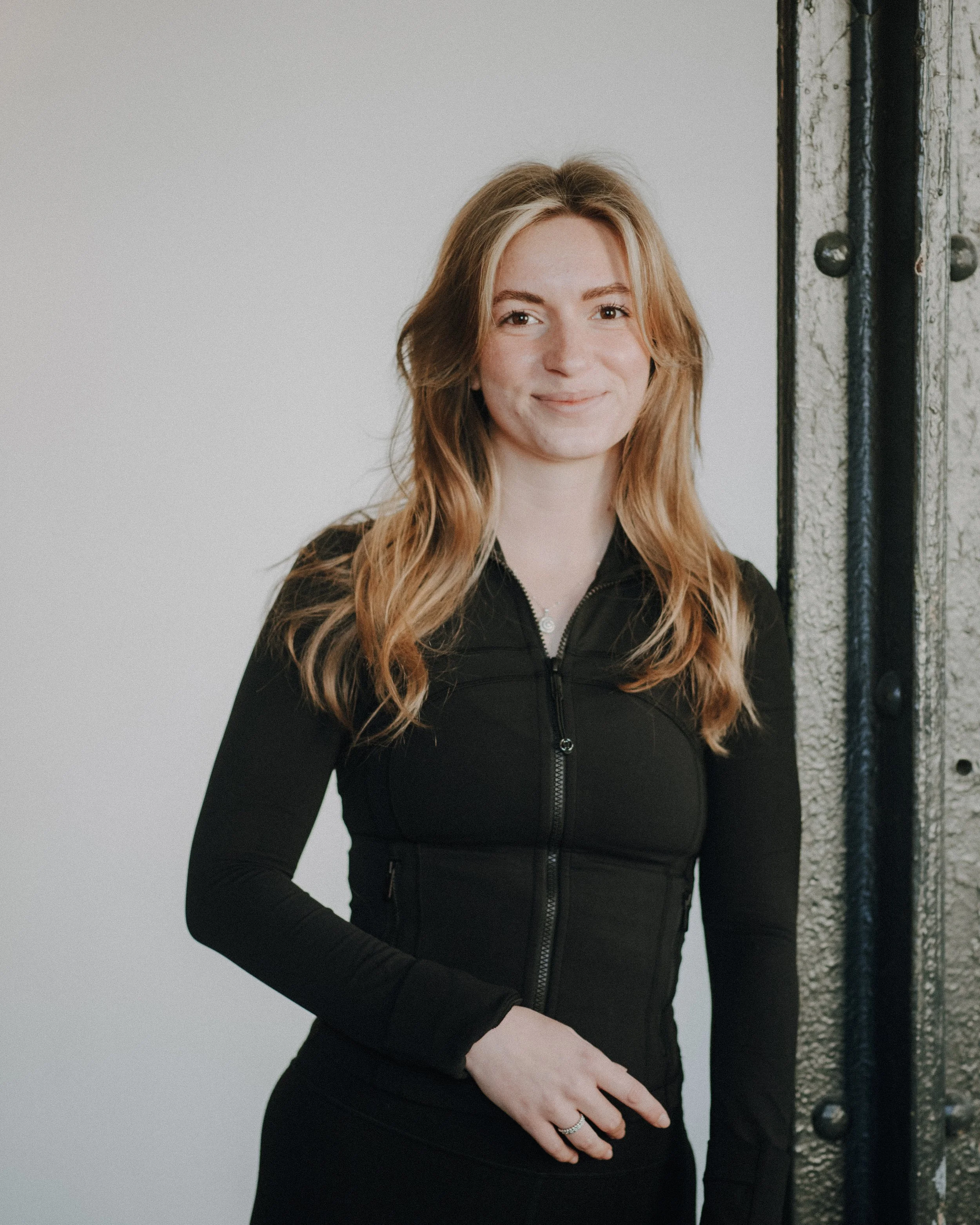 Schwarz-Weiß-Foto unserer Trainerin Virginia, die ein dunkles Stirnband und ein kurzes Yoha-Top trägt. Sie lächelt in die Kamera.