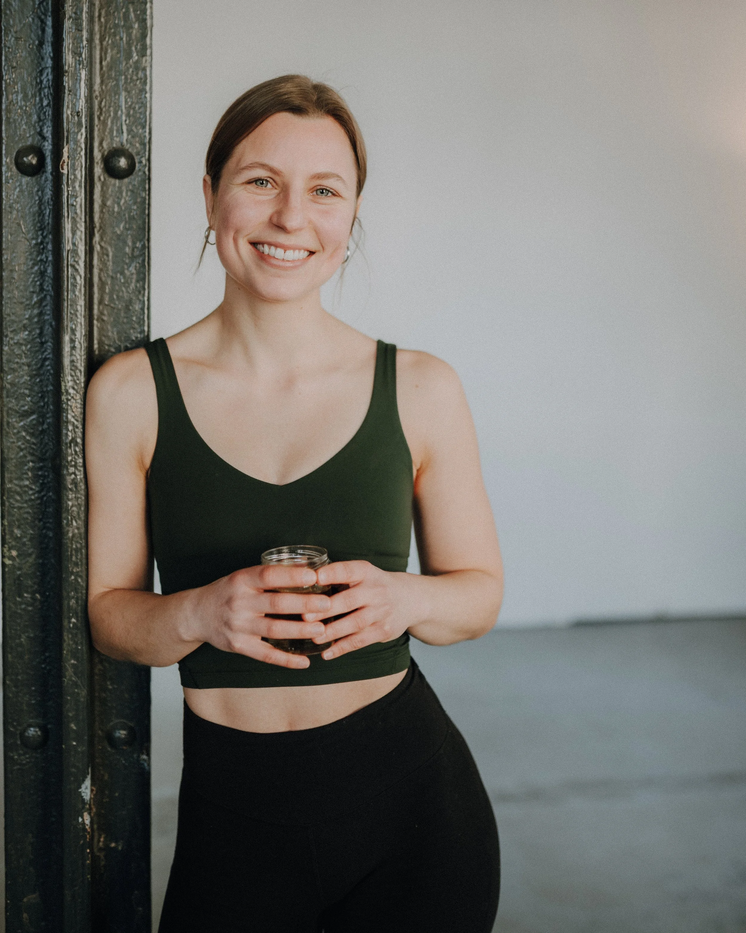 Unsere Trainerin Jessi mit strahlendem Lächeln in Sportkleidung vor neutralem Hintergrund.