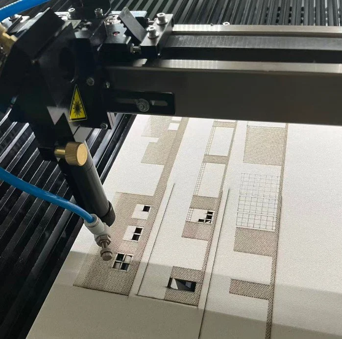 Laser cutting machine producing architectural model components with engraved surface patterns and cut-out openings.