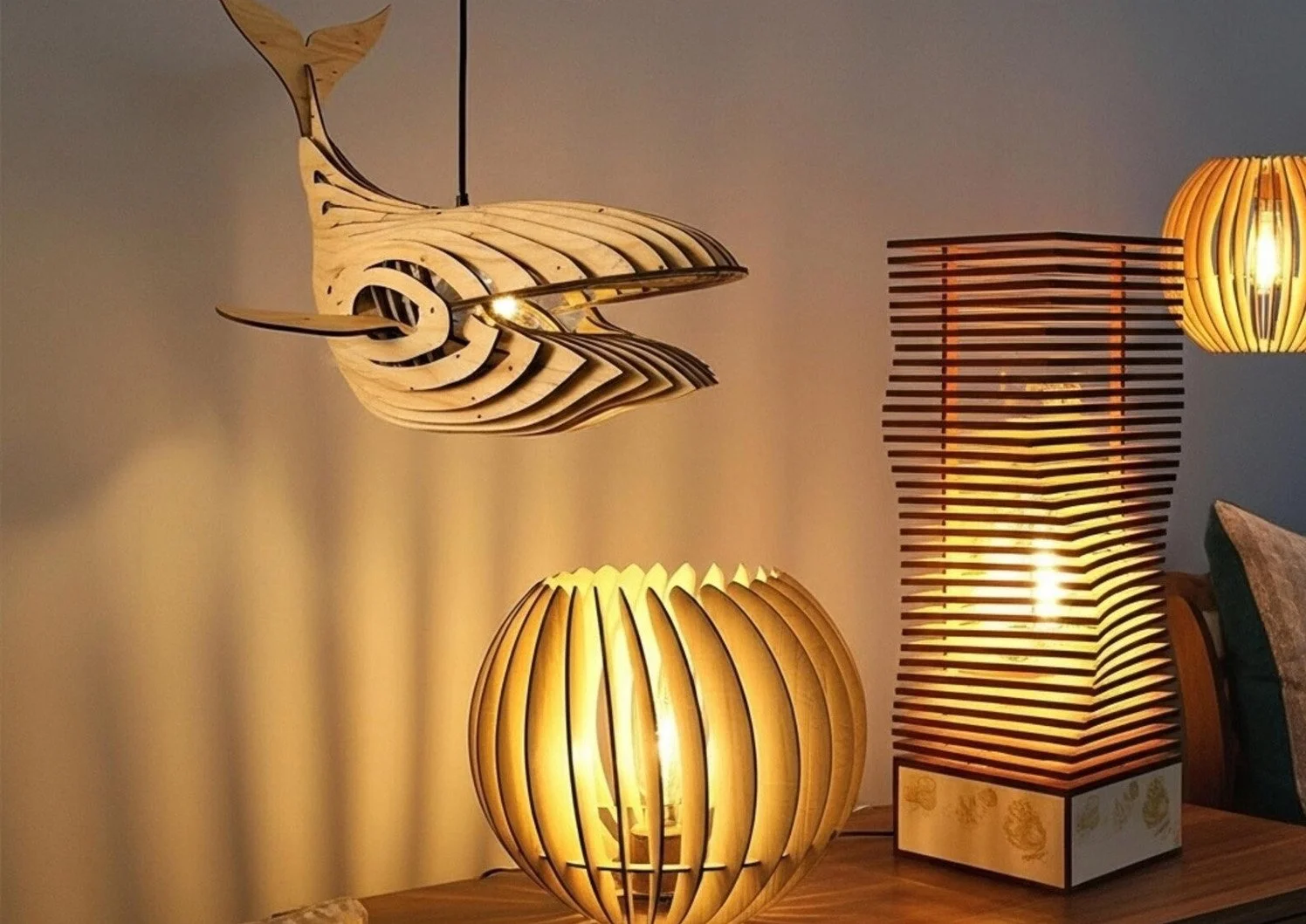 Laser-cut wooden lighting pieces and sculptural lamp designs, including a whale-shaped pendant light, a round table lamp and a layered floor lamp.