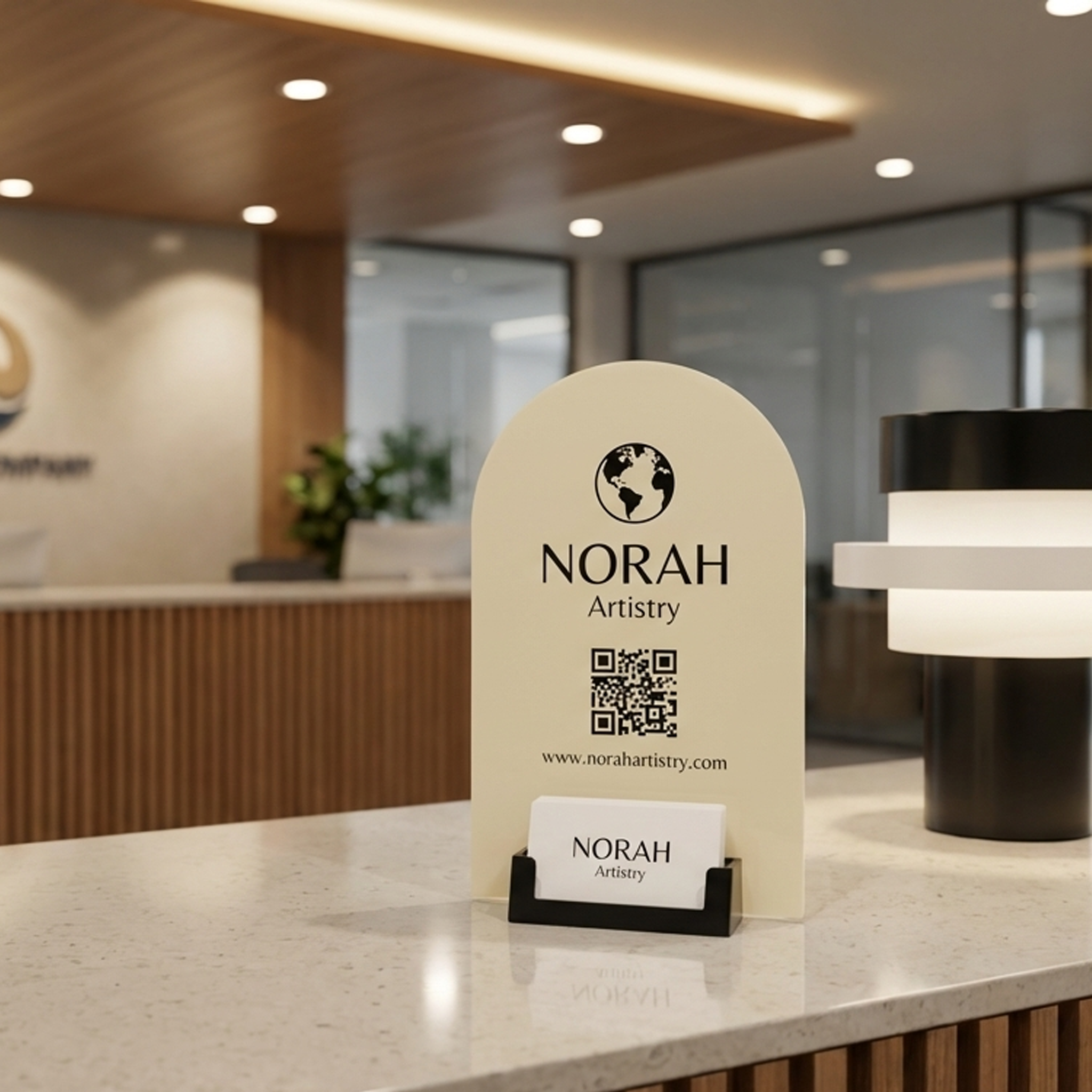 Reception desk sign for Norah Artistry, featuring a globe logo, a QR code, and a card holder with business cards, in a modern office setting.