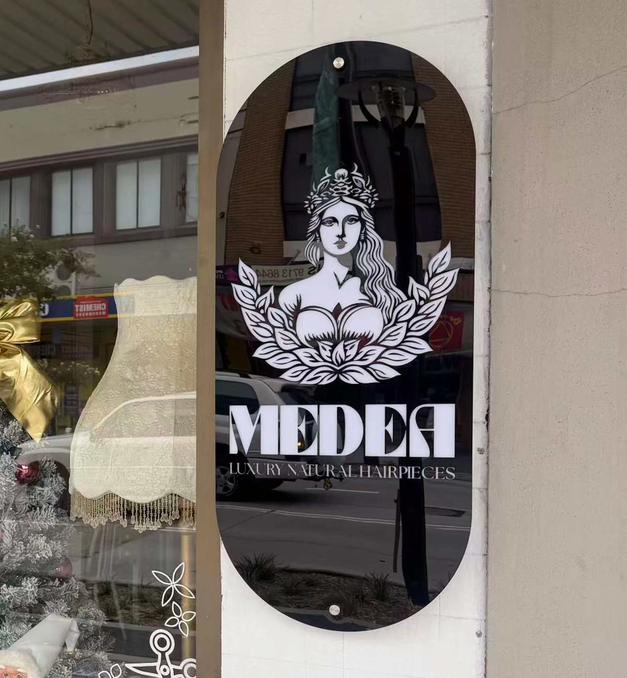 Custom oval shopfront window sign with white branding graphics and lettering mounted on a retail storefront