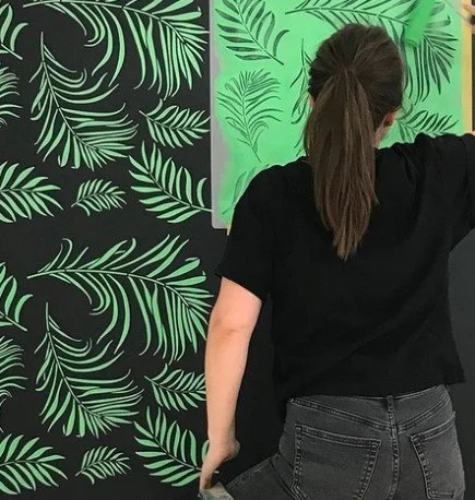 Decorative wall stencil being applied to create a repeating tropical leaf pattern mural