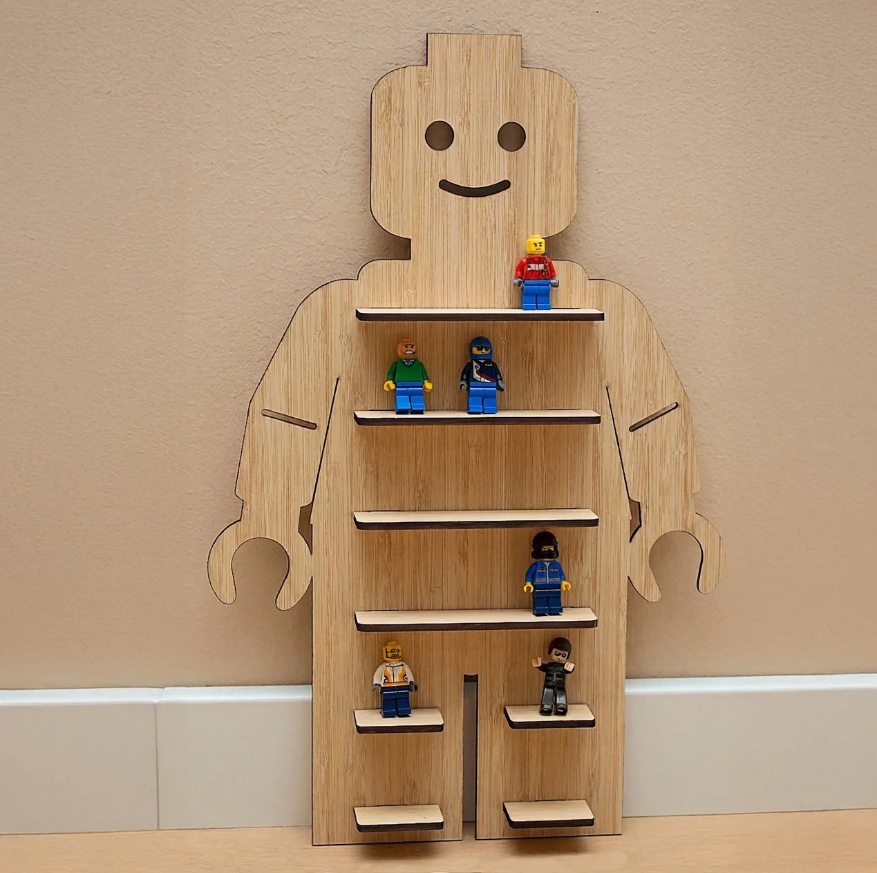 A wooden wall display shelf shaped like a minifigure, with small toy figures placed on staggered shelves.