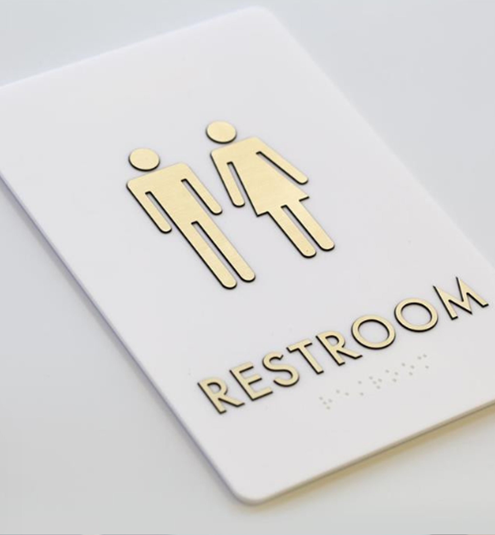 Minimal restroom sign with male and female icons and raised lettering on a white rectangular plaque