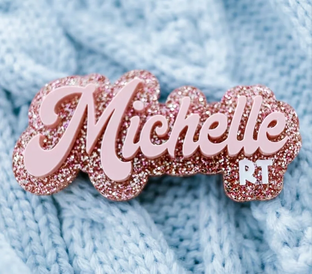 Personalised pink acrylic name badge with glitter backing and raised lettering shown in close-up