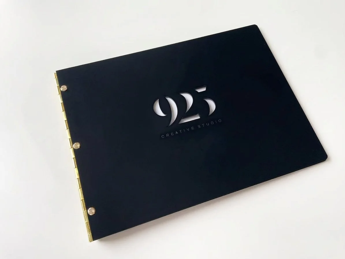 Black notebook or folder with a cut-out logo '25' and the words 'CREATIVE STUDIO' on the cover, laid on a white surface.