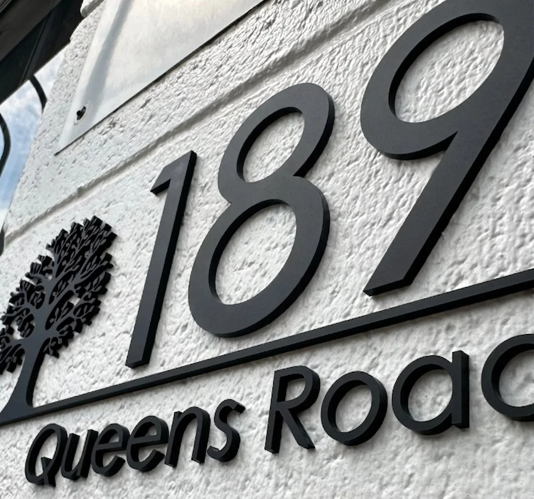 Modern exterior house number sign with raised black lettering mounted on a textured white wall