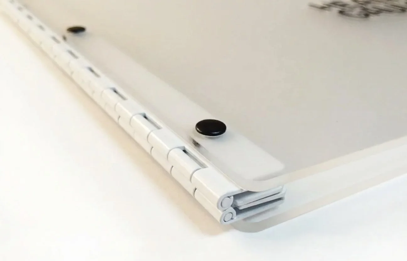 Close-up of a white dry erase whiteboard with a hinge in the corner and two black magnets attached.