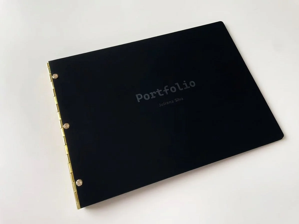 Black portfolio folder with gold accents and the words 'Portfolio' and 'Juliana Silva' on the cover.
