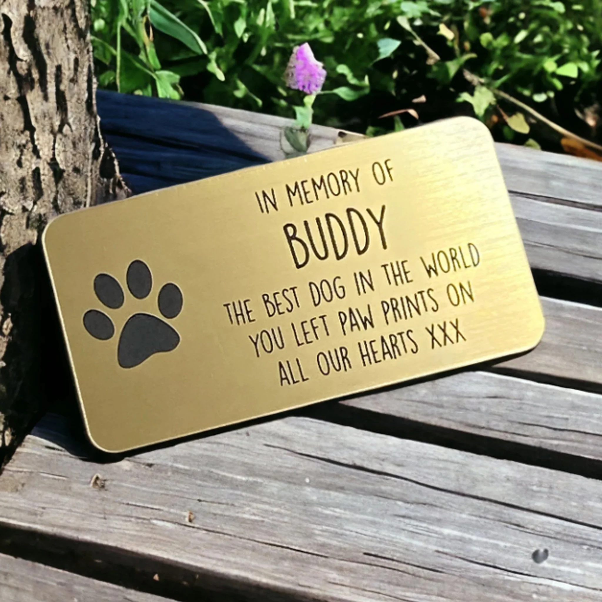 Engraved acrylic memorial plaque with personalised text and paw print detail placed on a wooden bench outdoors