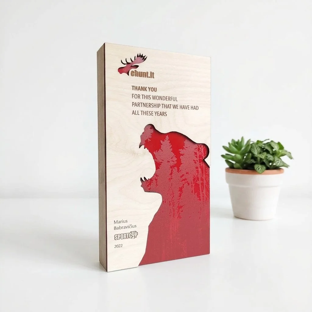 Custom layered timber recognition award with printed message and red graphic detail displayed on a tabletop beside a small plant