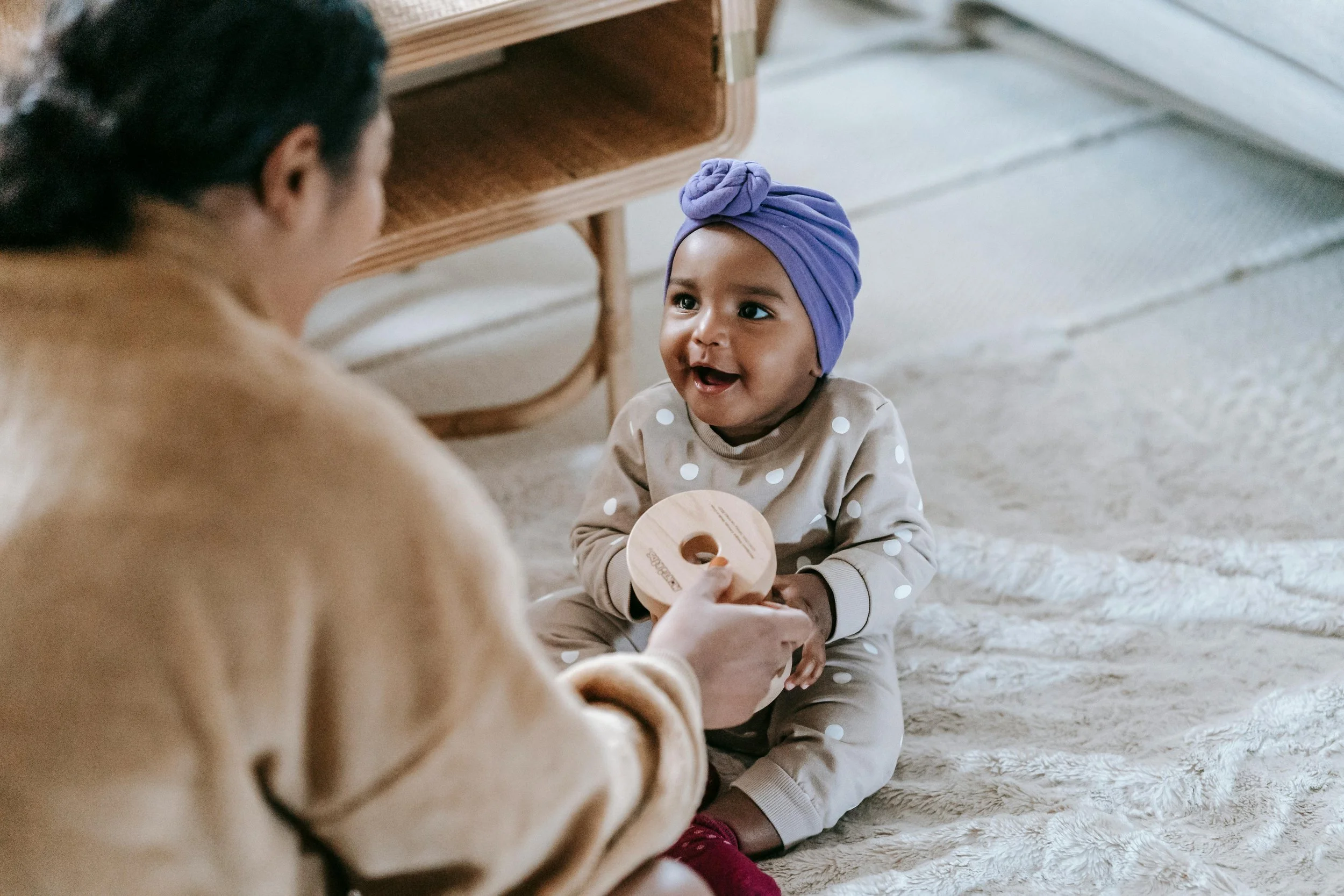 Mom handing baby a wooden circle with a hole in the middle. Baby has a purple headwrap on and is smiling. Infant and Toddler Development Circles in Niagara, Ontario with Heather Boyd