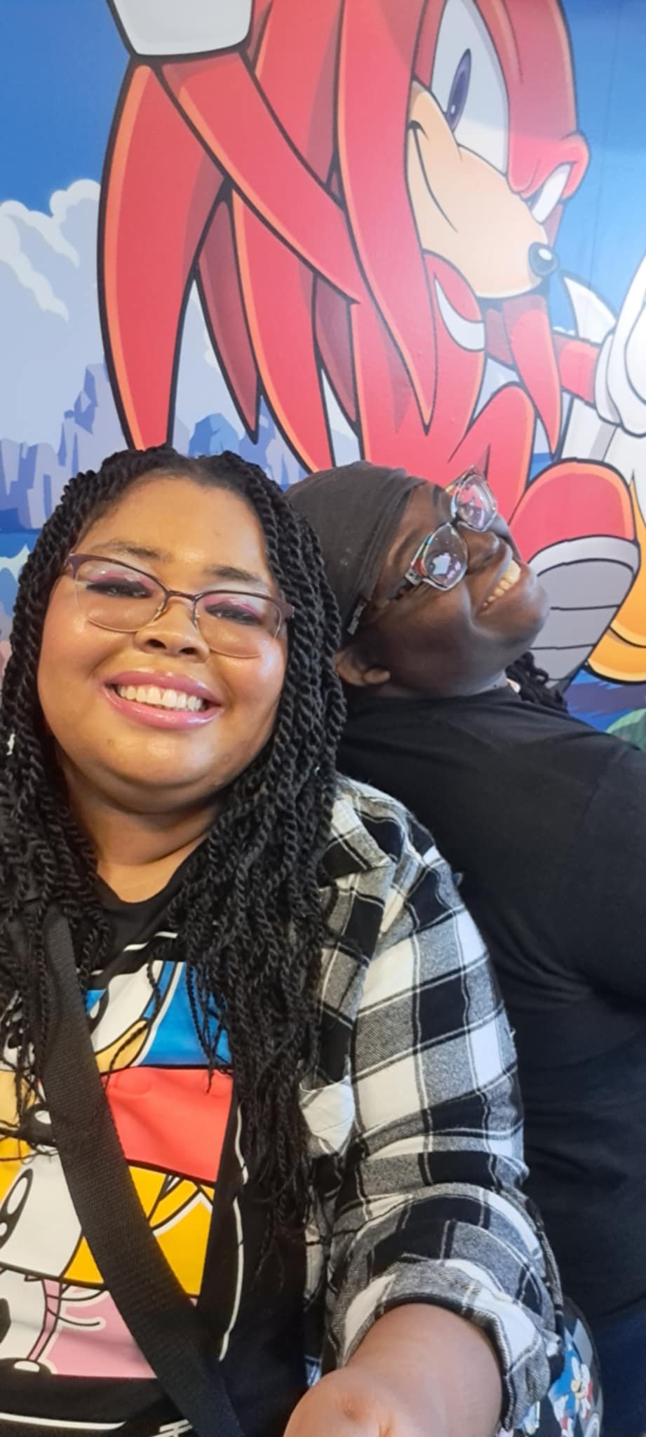 Two smiling women taking a selfie in front of a colorful mural featuring Sonic the Hedgehog.