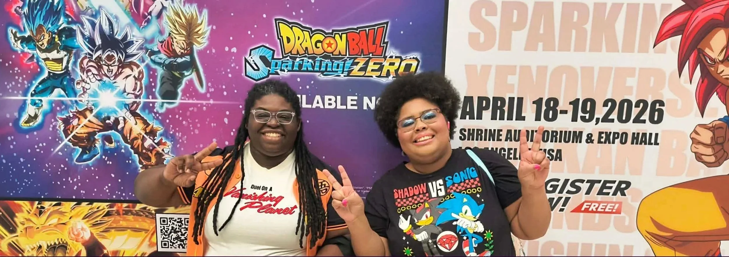 Two women smiling and posing at a convention, with a vibrant Dragon Ball themed backdrop featuring characters and event details.