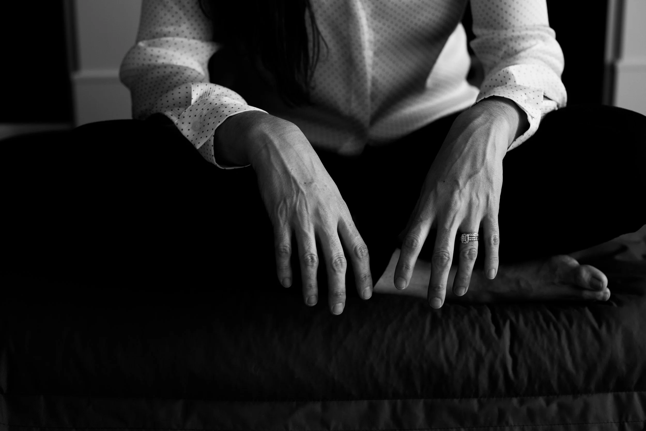 Black and white photograph of a woman's hands resting quietly, used to illustrate the therapeutic space in the OBH Matrescence Framework