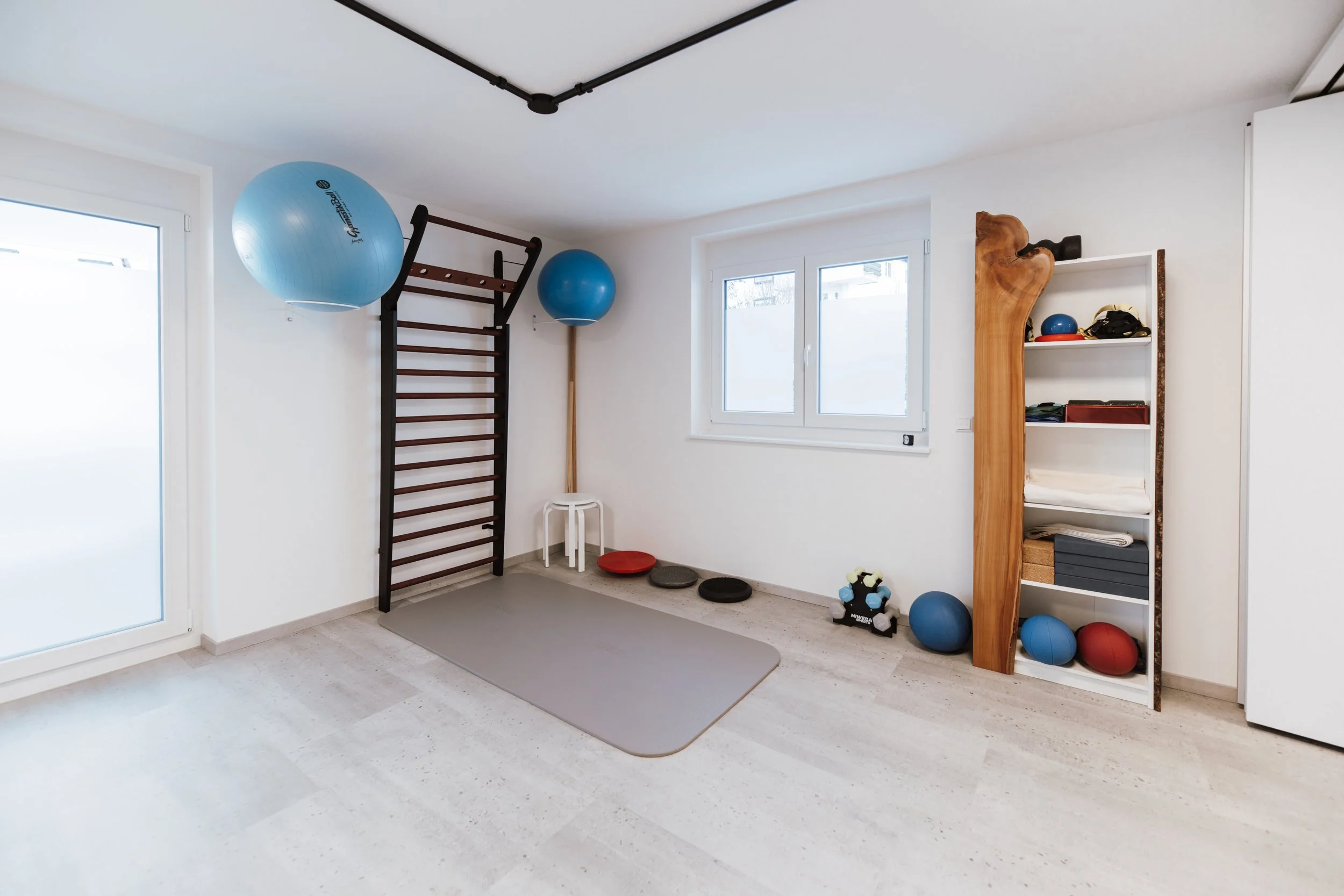 Ein Spielraum mit Turngerät, Gymnastikbällen, Matten und Spielsachen, in einem hellen Raum mit Fenstern.