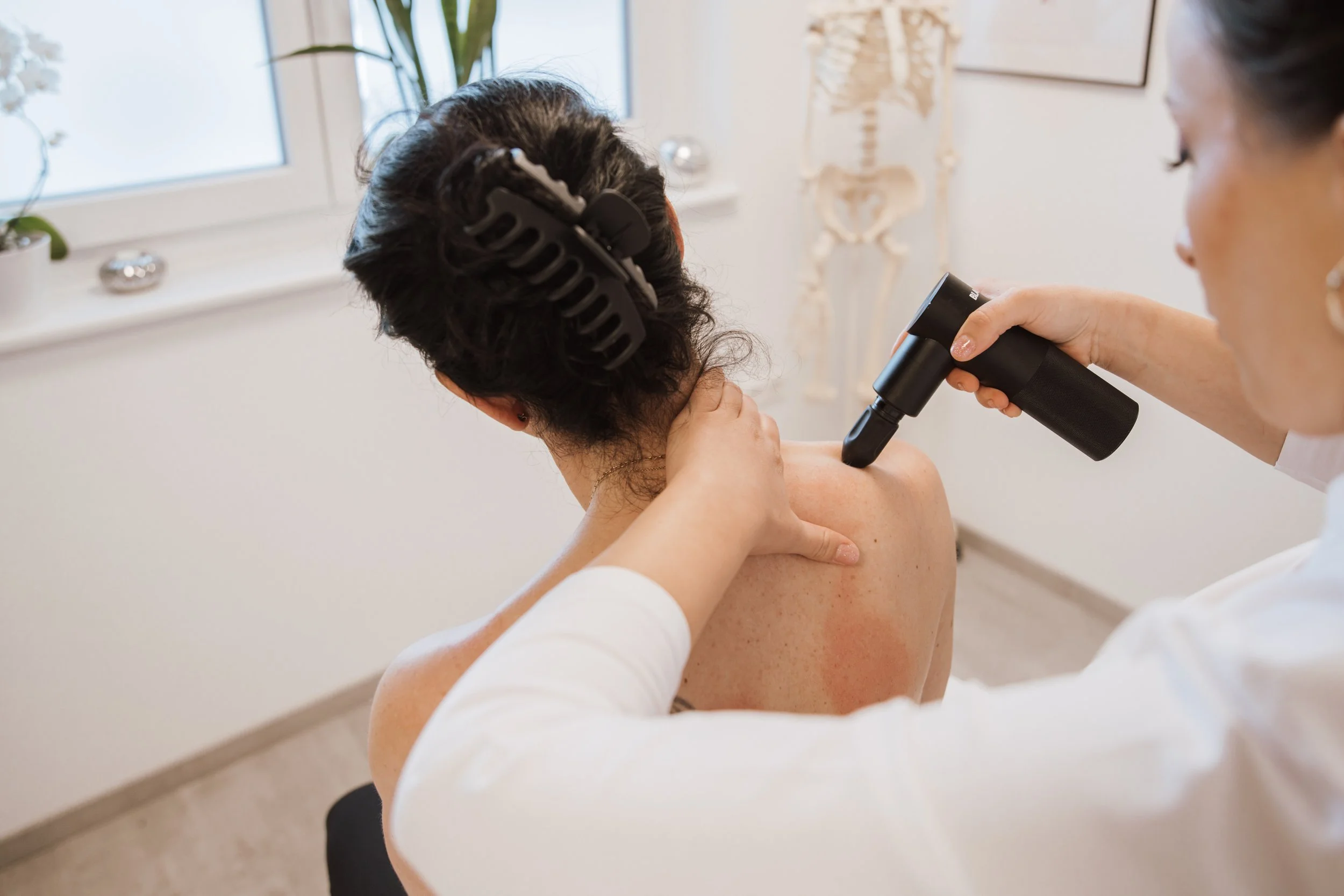 Ärztin behandelt Patientin mit Holstromy, die auf dem Rücken liegt, im Behandlungszimmer, mit Skelet kann im Hintergrund gesehen werden.