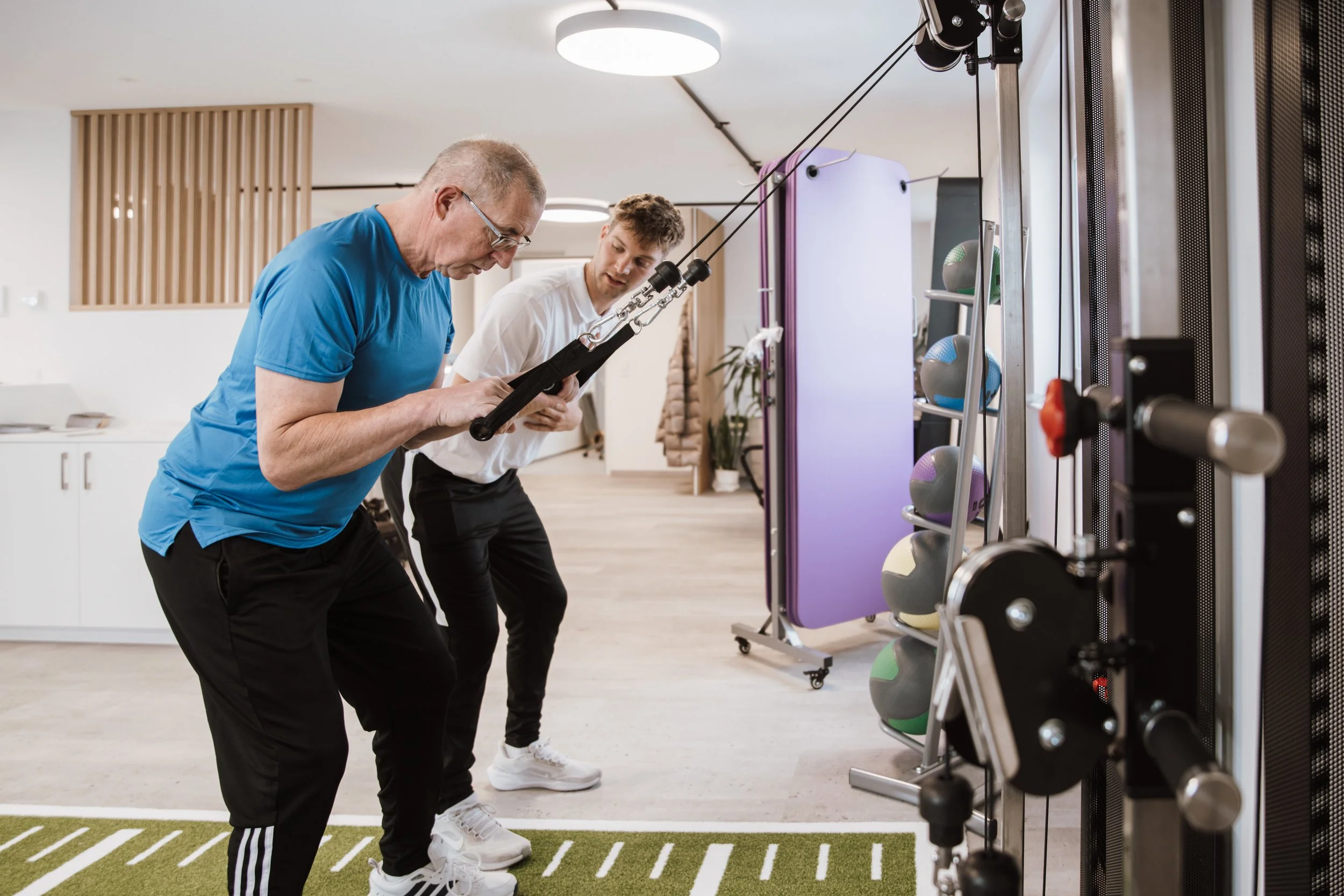Zwei Männer in einem Fitnessstudio, die mit Ringen an einem Spezialgerät trainieren.