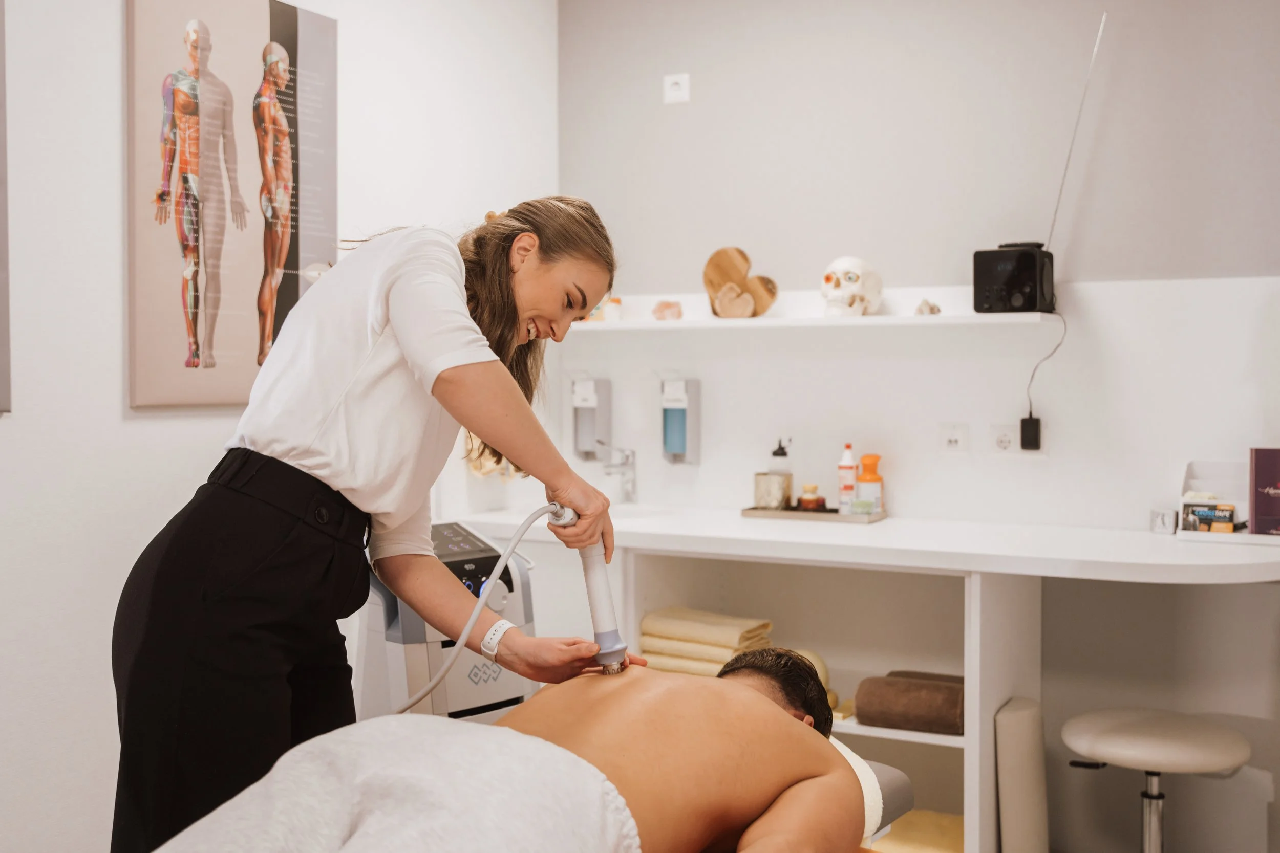 Ärztin führt eine medizinische Behandlung an einem nackten Mann auf einem Therapieliege durch, in einer medizinischen Praxis mit medizinischem Equipment und anatomischen Postern.